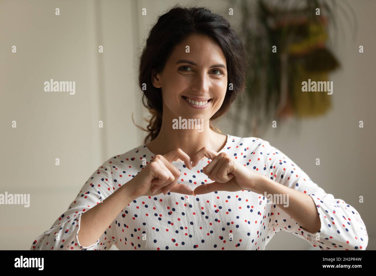 Feliz mujer hispana agradecida haciendo gesto de corazón en el dedo Foto de stock