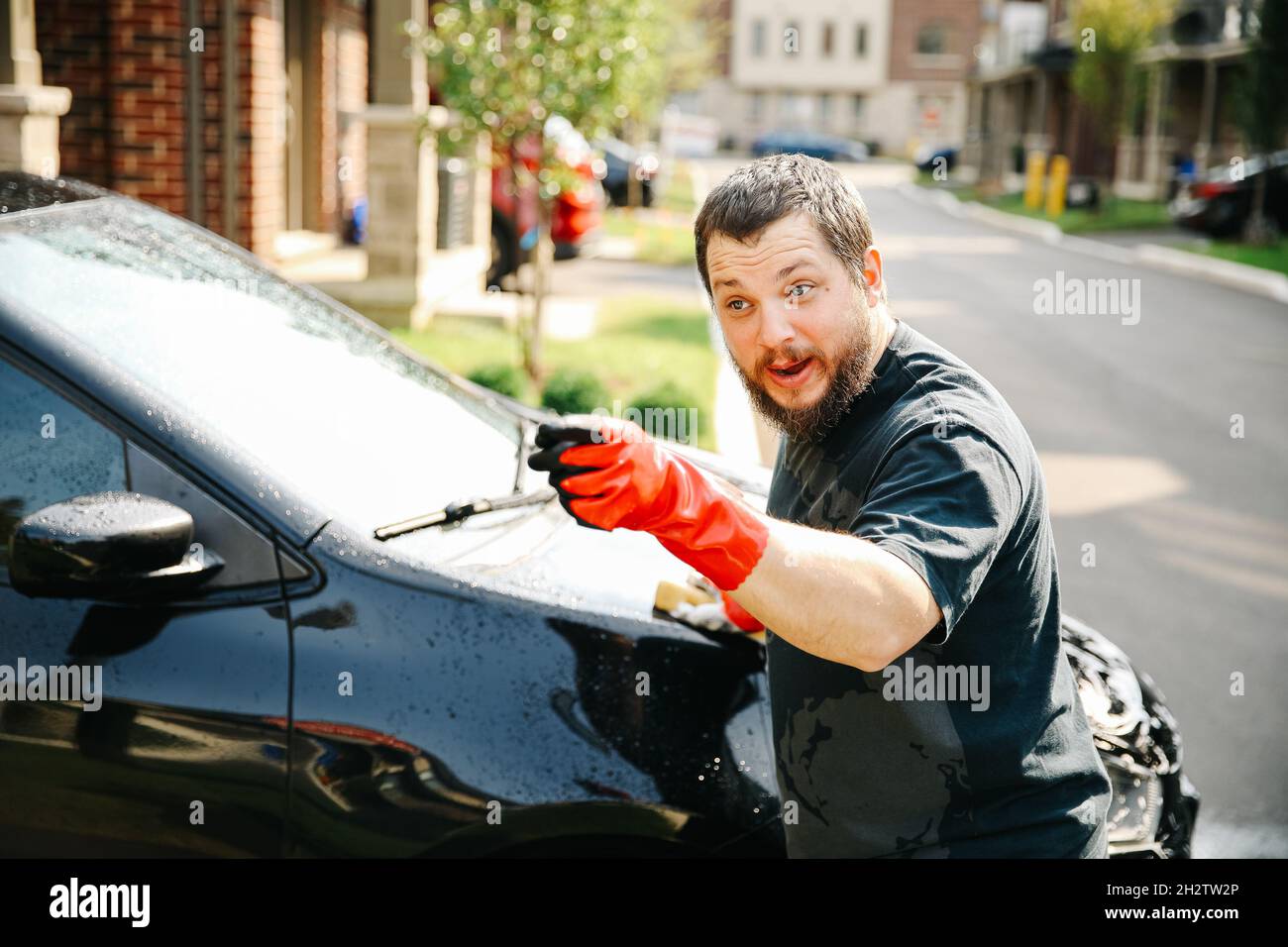 Hombre Americano lavando su propio coche negro afuera con esponja y usando guantes  rojos apuntando el dedo Fotografía de stock - Alamy