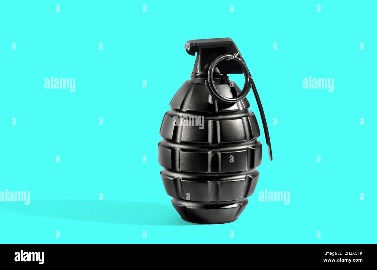 Una granada de metal negro sin explotar con alfiler redondo sobre fondo cian con sombra larga y espacio de copia Foto de stock