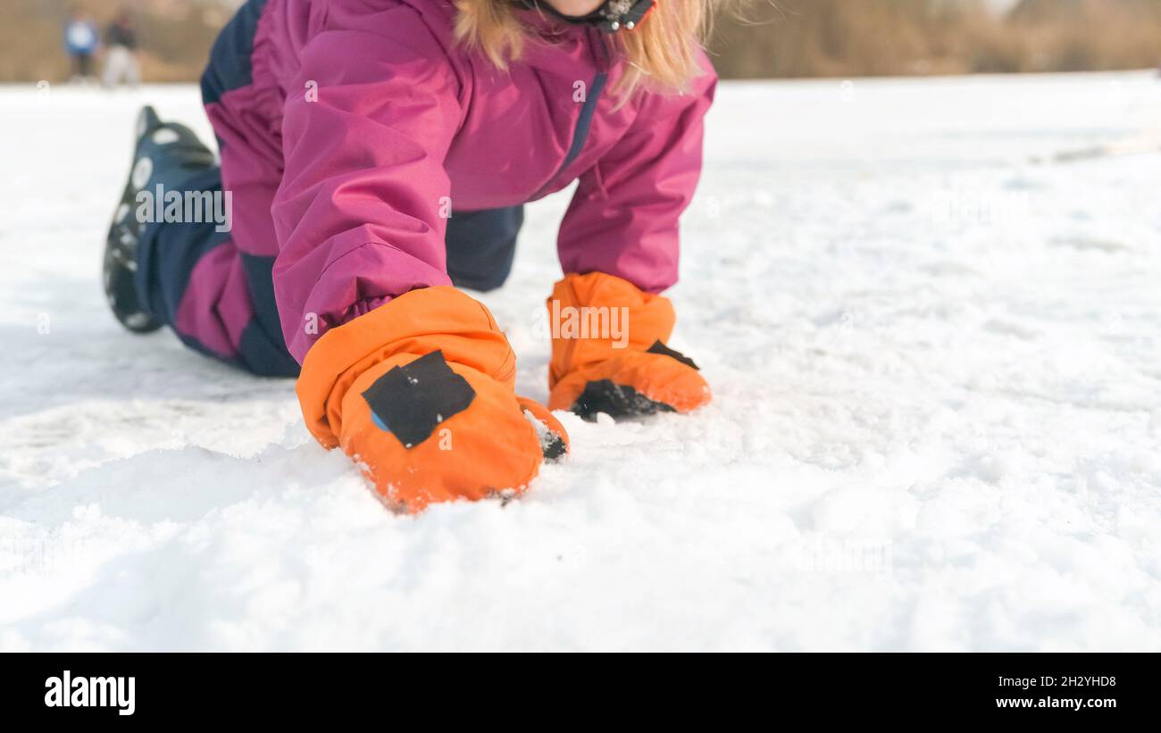 Niña con traje de nieve, casco y guantes impermeables, arrodillándose y  jugando con la nieve Fotografía de stock - Alamy