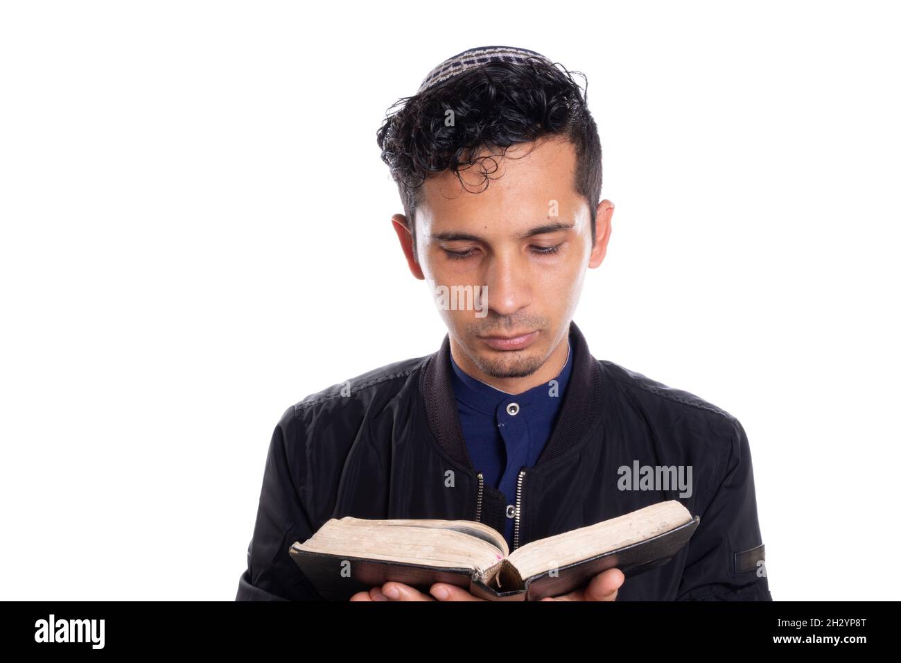 Hombre latino que practica el judaísmo aislado sobre fondo blanco. Joven con kippah leyendo la biblia. Foto de stock