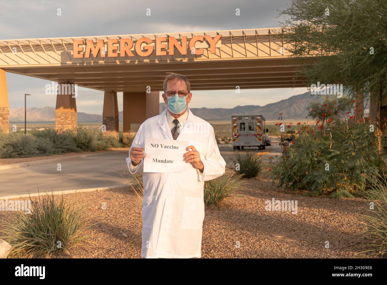 El médico en la capa blanca y la máscara sostiene el signo anti-vacuna frente a la caída de emergencia Foto de stock