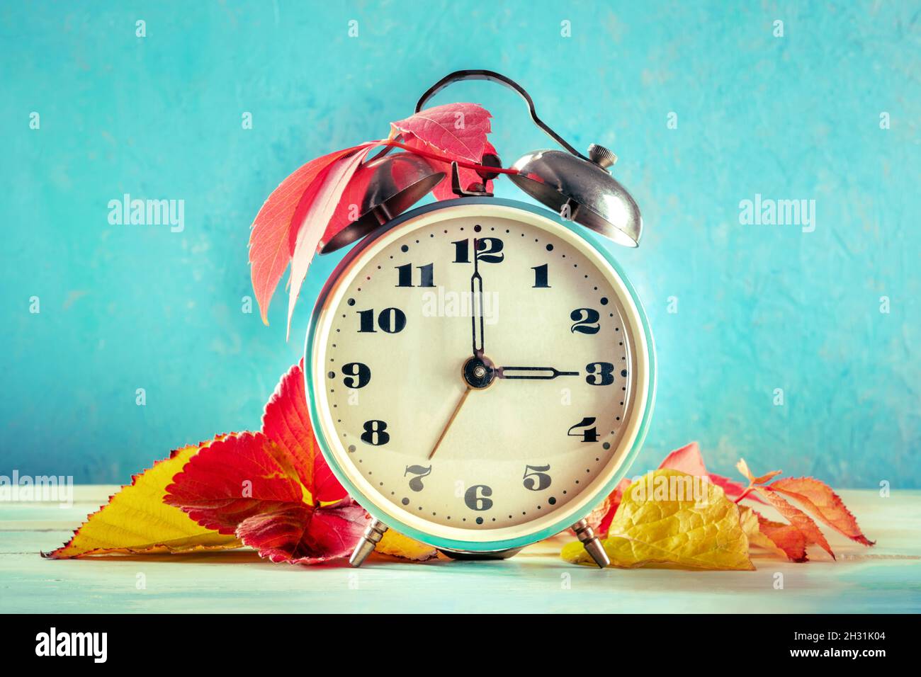 Concepto de horario de verano, otoño atrás en otoño. Un reloj despertador  vintage con hojas otoñales sobre un fondo de color verde azulado Fotografía  de stock - Alamy
