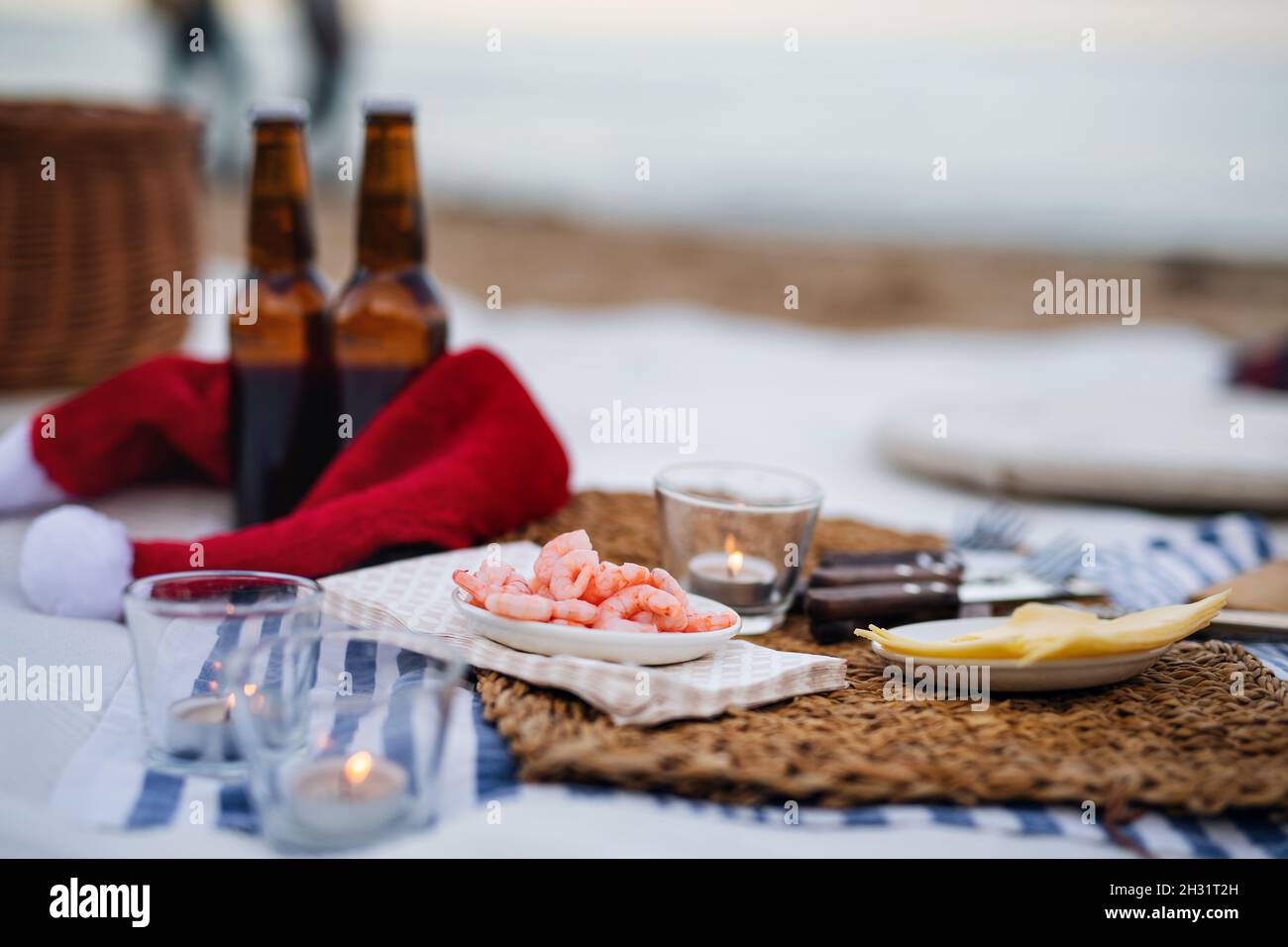 Picnic en la playa con chiripms, cerveza, velas y sombrero de santa. Año nuevo exótico y Navidad Foto de stock