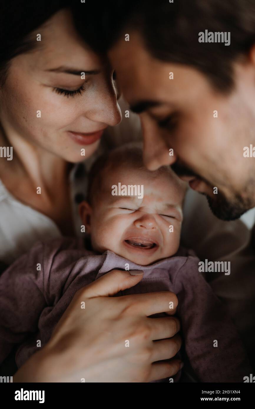 Cerca de los padres jóvenes sosteniendo y besando a su bebé recién nacido en casa Foto de stock