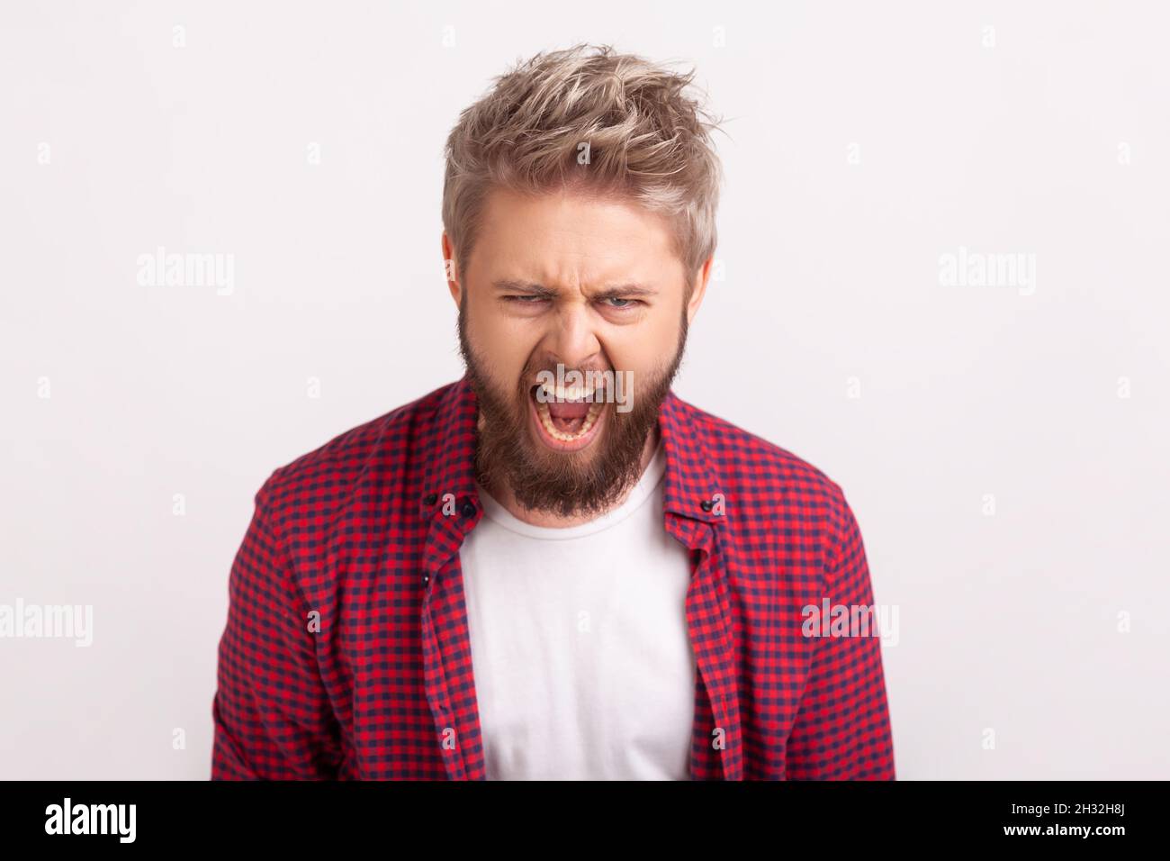 Retrato de un joven disgustado con barba gritando mirando la cámara, expresando enojo e irritación, mal humor. Estudio en interior grabado aislado sobre fondo gris Foto de stock