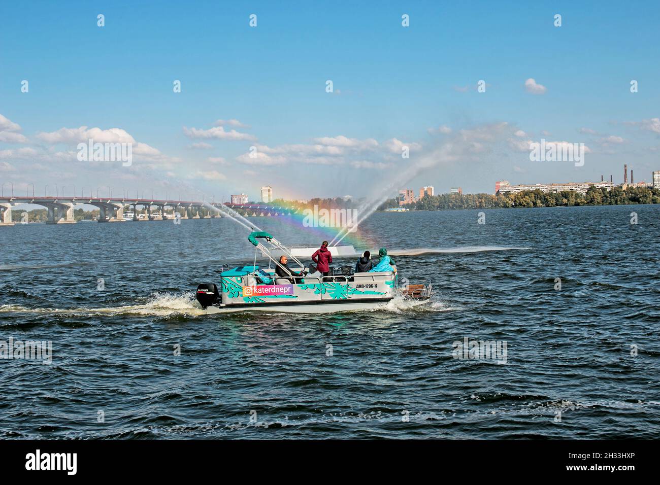 Dnepropetrovsk, Ucrania - 10.05.2021: Los habitantes de la ciudad en un barco de placer admirar la fuente con un hermoso arco iris. Fondo azul cielo. Arco iris de Foto de stock