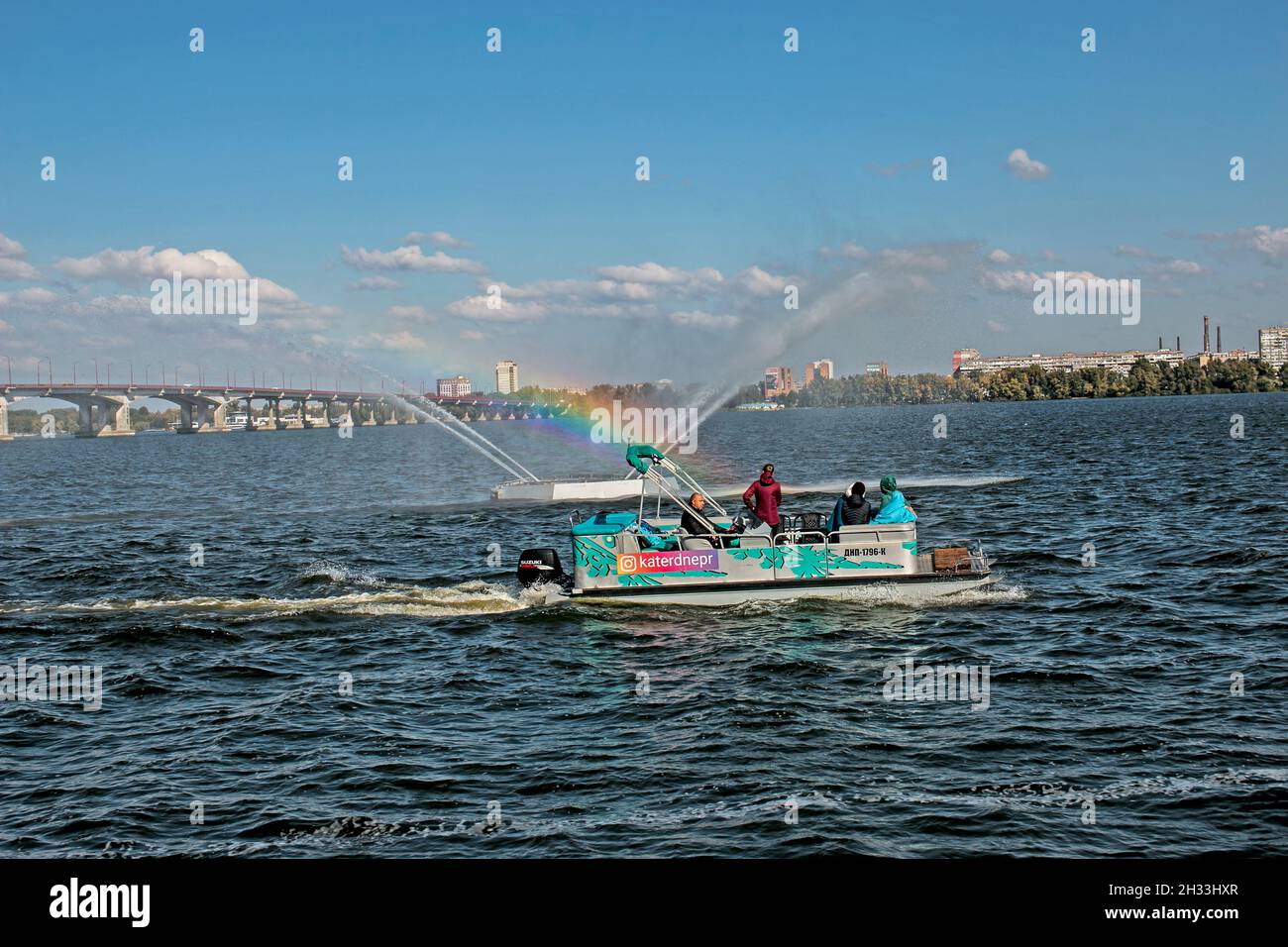 Dnepropetrovsk, Ucrania - 10.05.2021: Los habitantes de la ciudad en un barco de placer admirar la fuente con un hermoso arco iris. Fondo azul cielo. Arco iris de Foto de stock