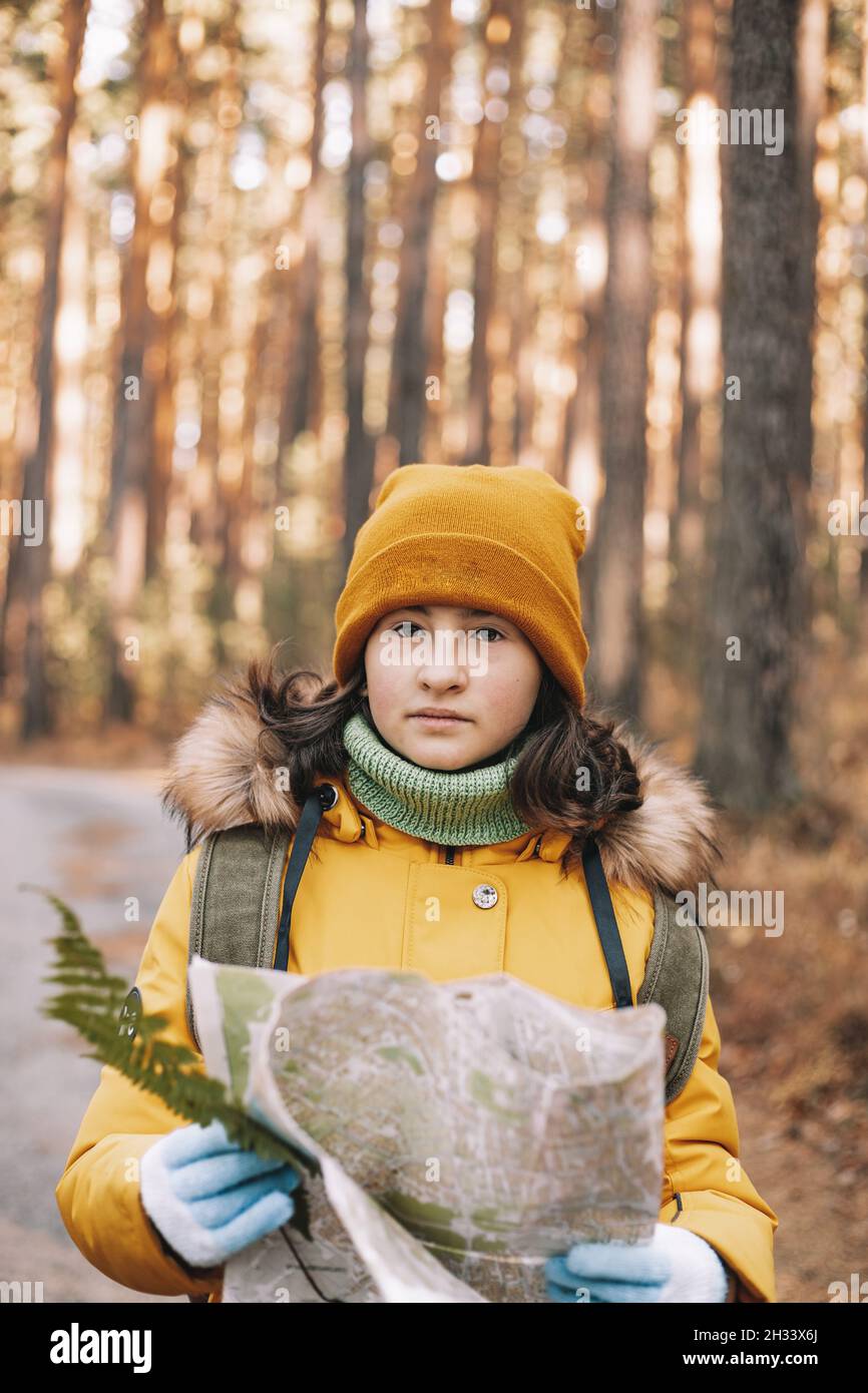 Linda chica caucásica está haciendo senderismo en el bosque de pinos de otoño. Un adolescente con una mochila y un mapa camina a lo largo de la ruta. Actividades al aire libre. Disparo vertical Foto de stock