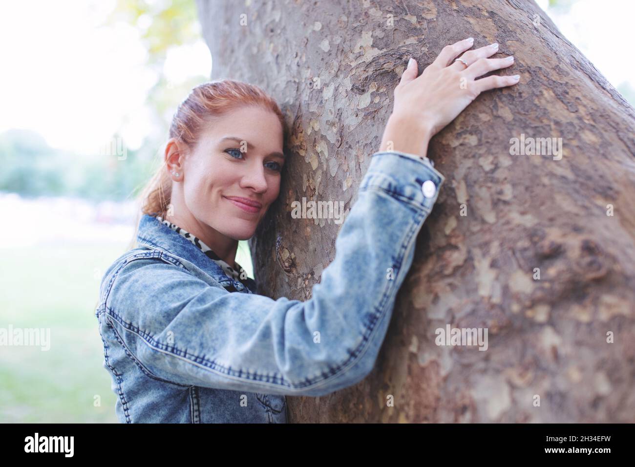 Feliz joven natural pelirroja mujer caucásica abrazando el árbol en la naturaleza Foto de stock