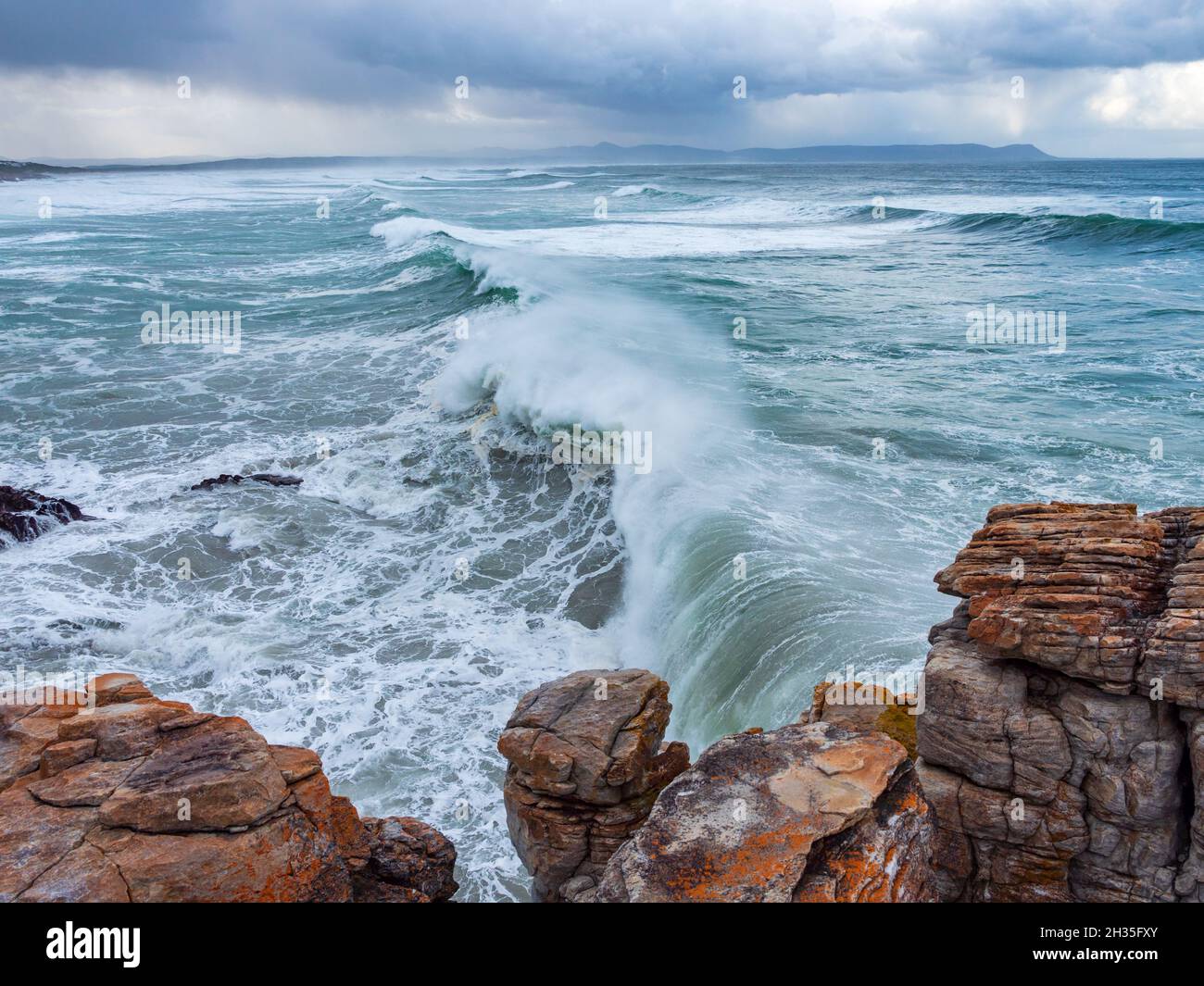 Enormes olas rompiendo sobre una costa rocosa bajo un cielo en medio de la cría. Sievers Point (Sieverspunt) Hermanus. Costa de las Ballenas. Overberg. Cabo Occidental. Sur de África Foto de stock