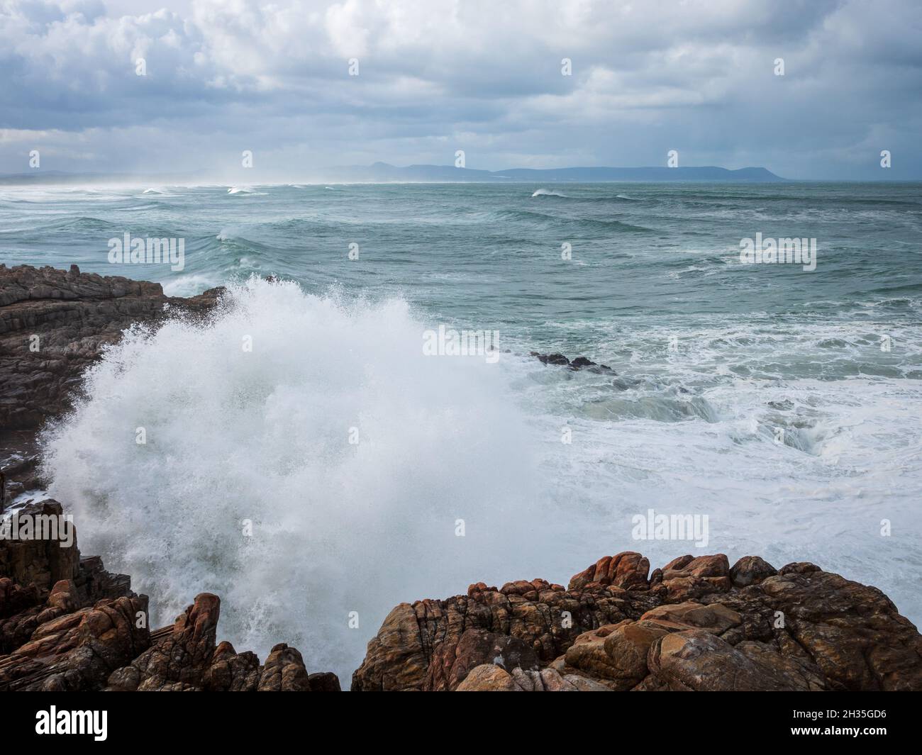 Enormes olas rompiendo sobre una costa rocosa bajo un cielo en medio de la cría. Sievers Point (Sieverspunt) Hermanus. Costa de las Ballenas. Overberg. Cabo Occidental. Sur de África Foto de stock