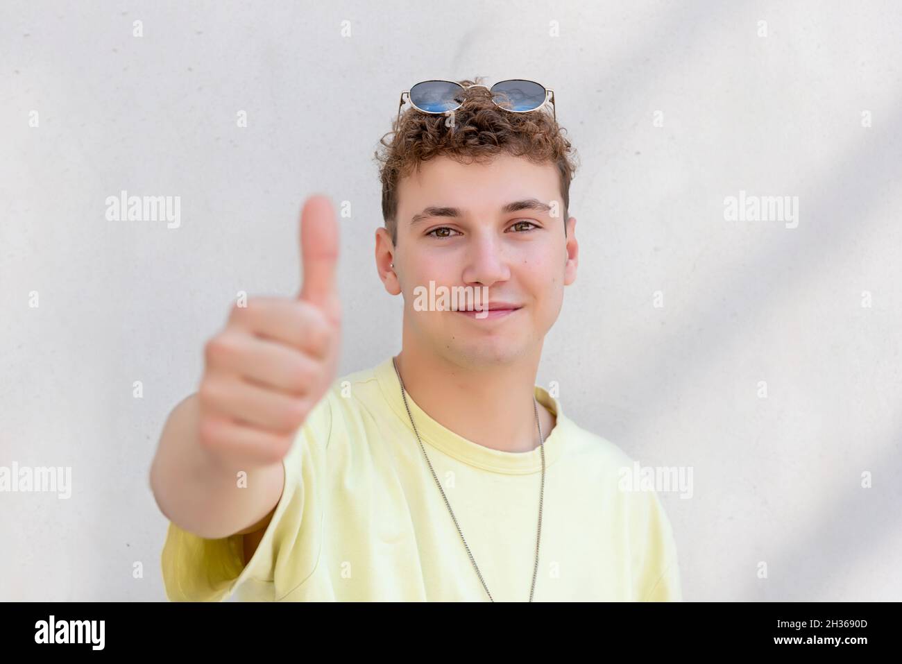 Hombre joven en una camiseta amarilla con gafas en la cabeza levantando el pulgar hacia arriba