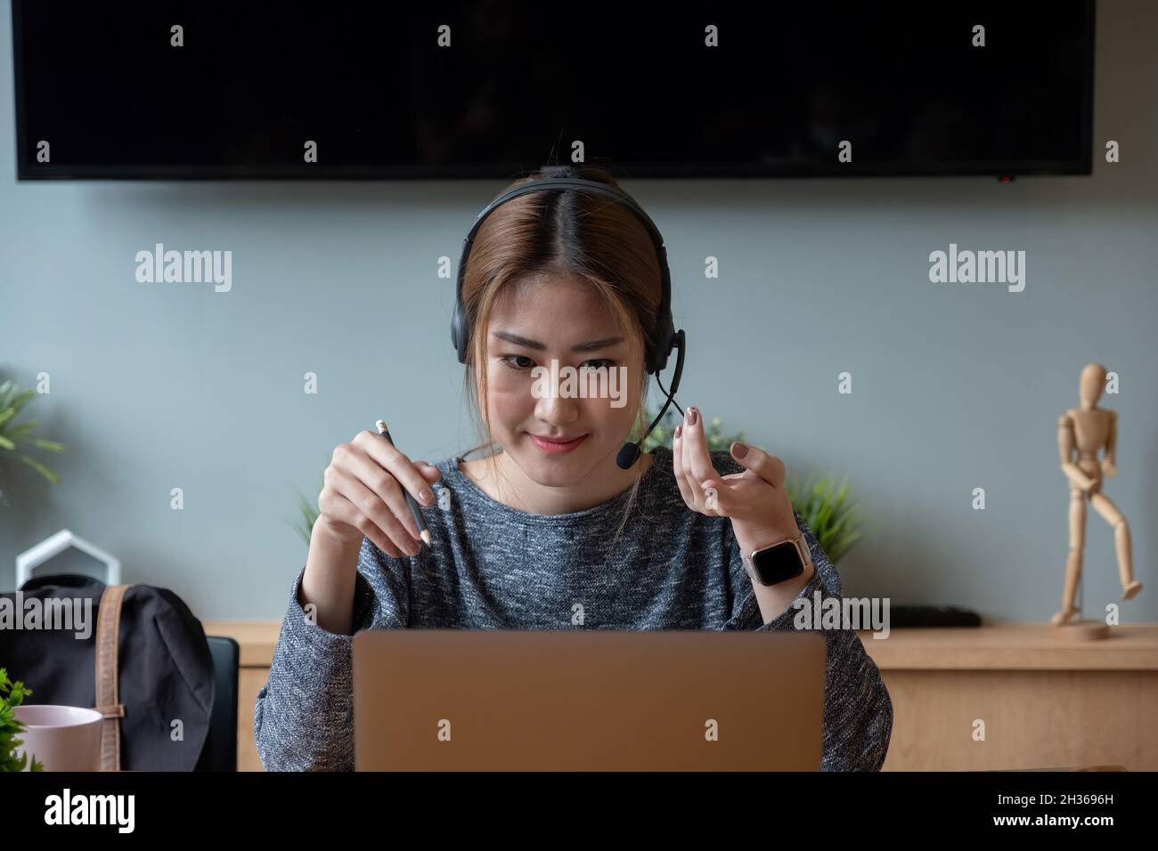 Fotografió a una sonriente mujer asiática independiente con auriculares, comunicándose con el cliente a través de una videollamada. Milenaria agradable tutor profesional Foto de stock