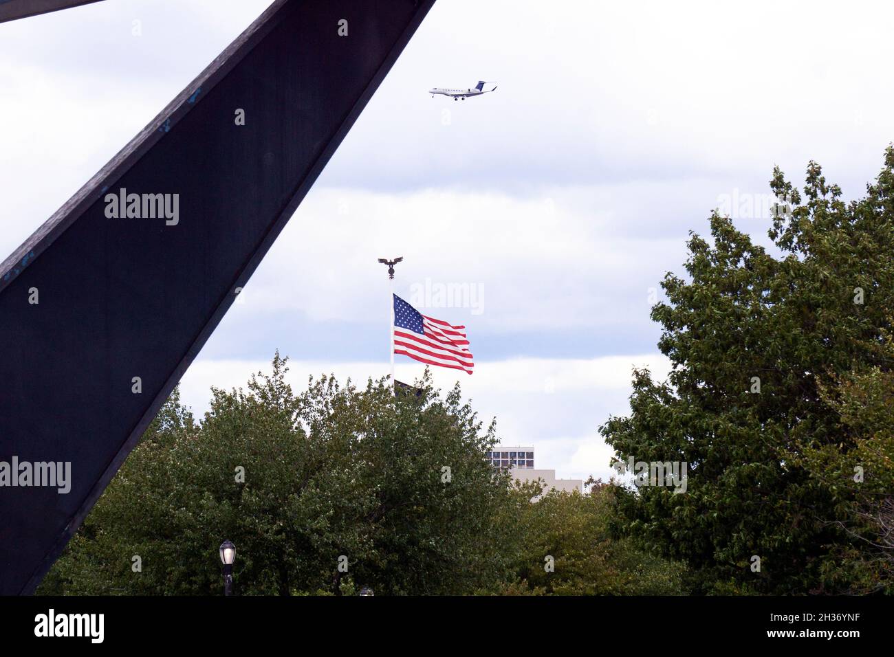 Una bandera americana y un avión visto a través del Unisphere en Flushing Meadows Corona Park en Queens, Nueva York. Foto de stock