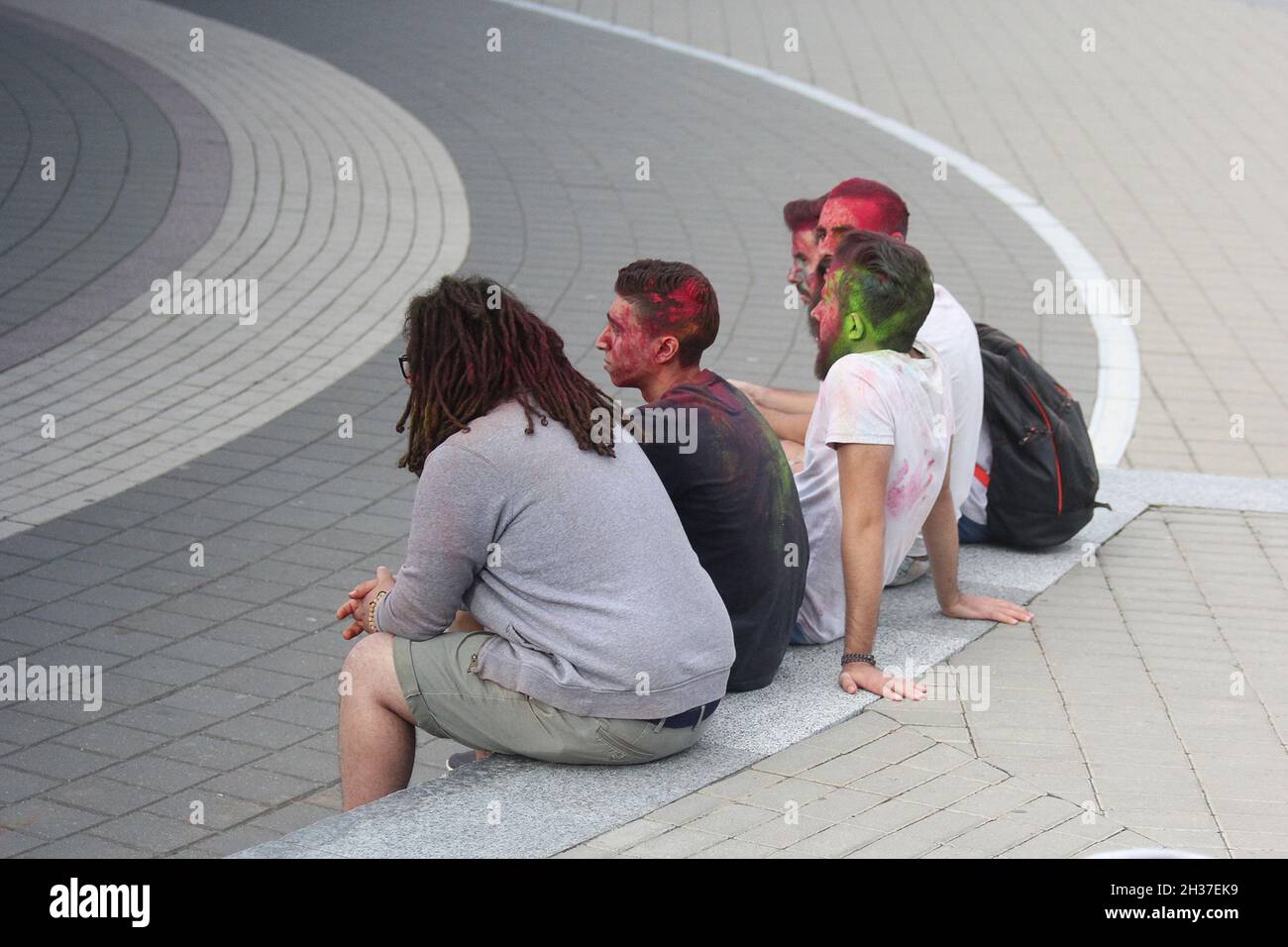 Fotografía editorial. Los hombres se sientan en el banco, las caras cubiertas con pintura de color después del festival holi . 3 de septiembre de 2016, Minsk Foto de stock