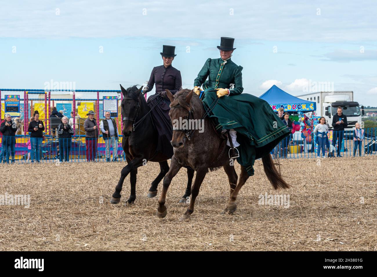 Dos mujeres en traje de época haciendo una exhibición de equitación en silla de montar a caballo en un evento de caballos, Reino Unido Foto de stock