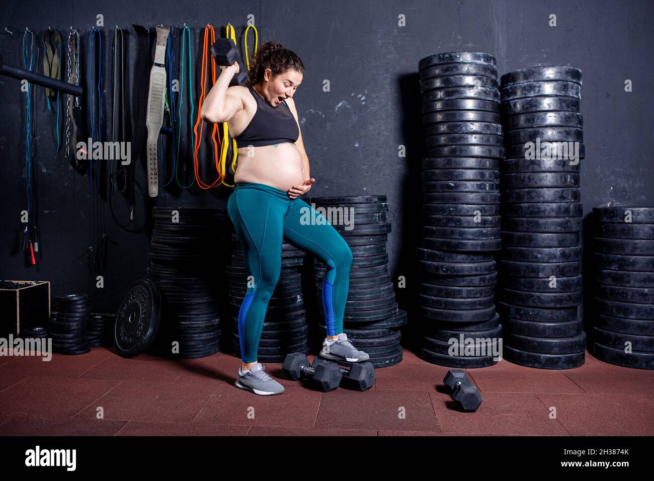 Mujer embarazada fuerte posando con pesas en sus manos contra fondo de  equipo deportivo en el gimnasio. Entrenamientos y ejercicios para mujeres  embarazadas en Fotografía de stock - Alamy