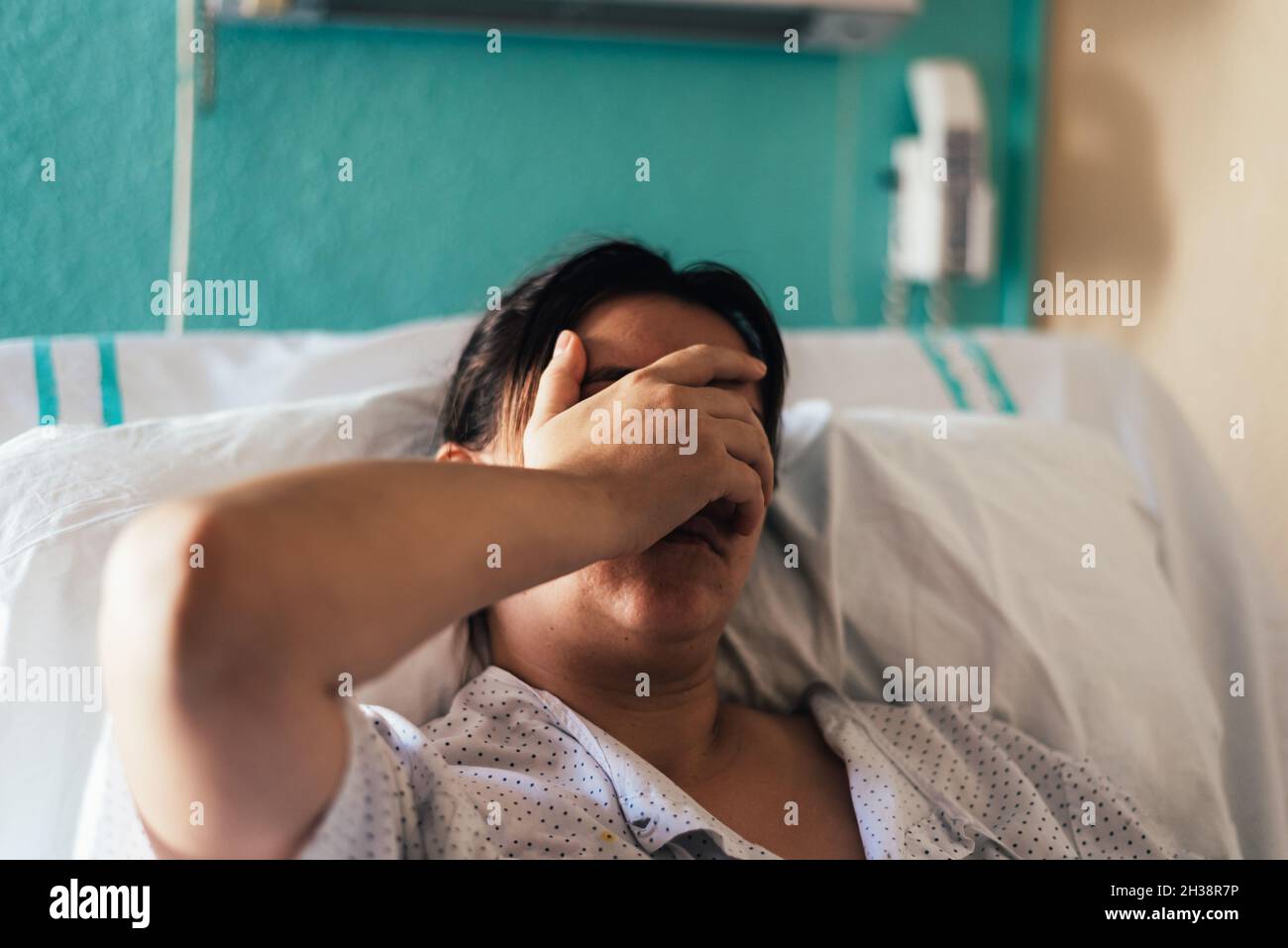 Una joven hospitalizada en una cama. Gestos de dolor y preocupación. Foto de stock