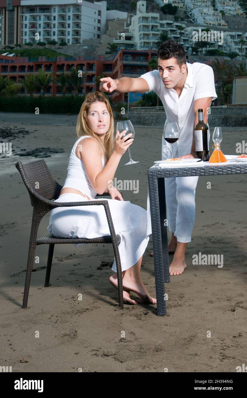 Pareja joven vestida de blanco celebrando una cena romántica en la playa  Fotografía de stock - Alamy