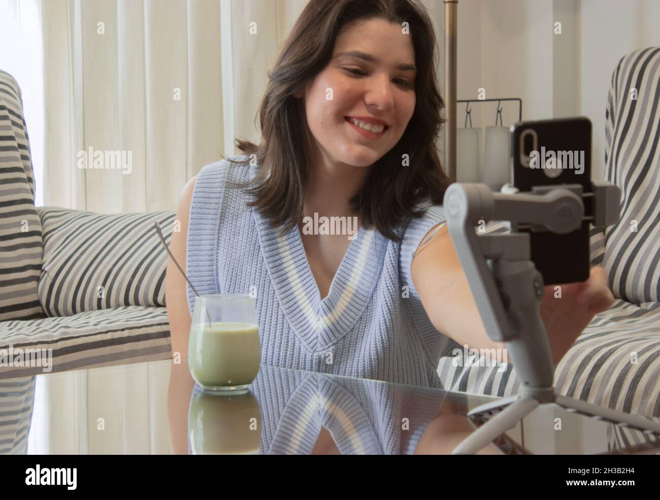 Una mujer joven disfruta matcha latte mientras inicia una videollamada con sus familiares para felicitarlos en Navidad y no poder estar juntos Foto de stock