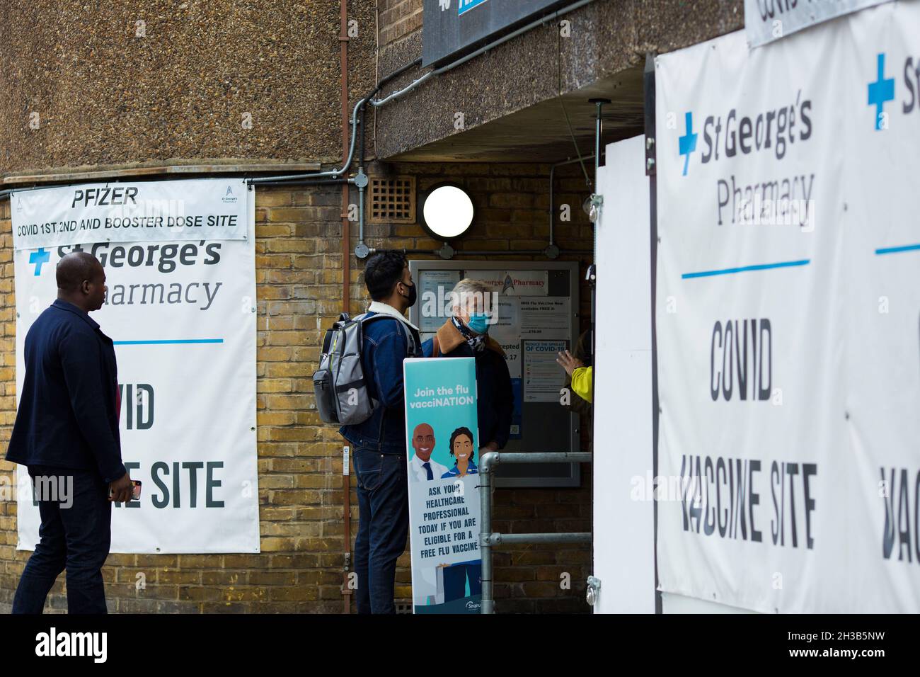 Las banderas de un sitio de vacuna de Covid se ven expuestas fuera de una farmacia cuando la gente llega a Londres, el 23 de octubre de 2021. Foto de stock