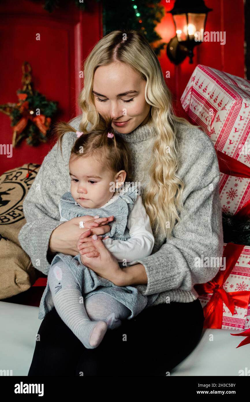 Tierna mamá bonita abraza a su hija en el fondo de Navidad. Vacaciones familiares, regalos, Navidad, concepto de Navidad Foto de stock