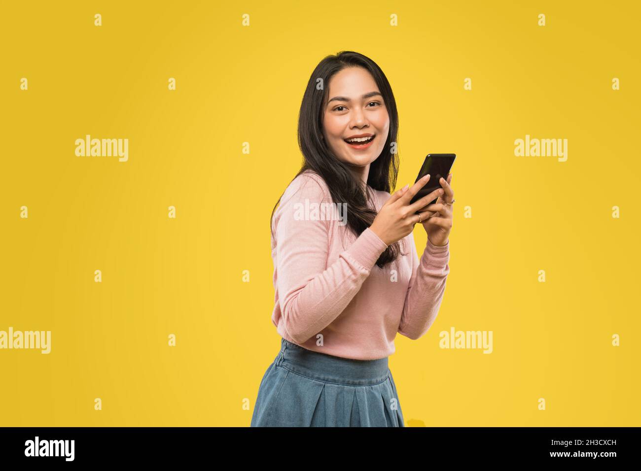 mujer atractiva con pelo suelto sonriendo mientras tecleaba el mensaje con el teléfono móvil Foto de stock