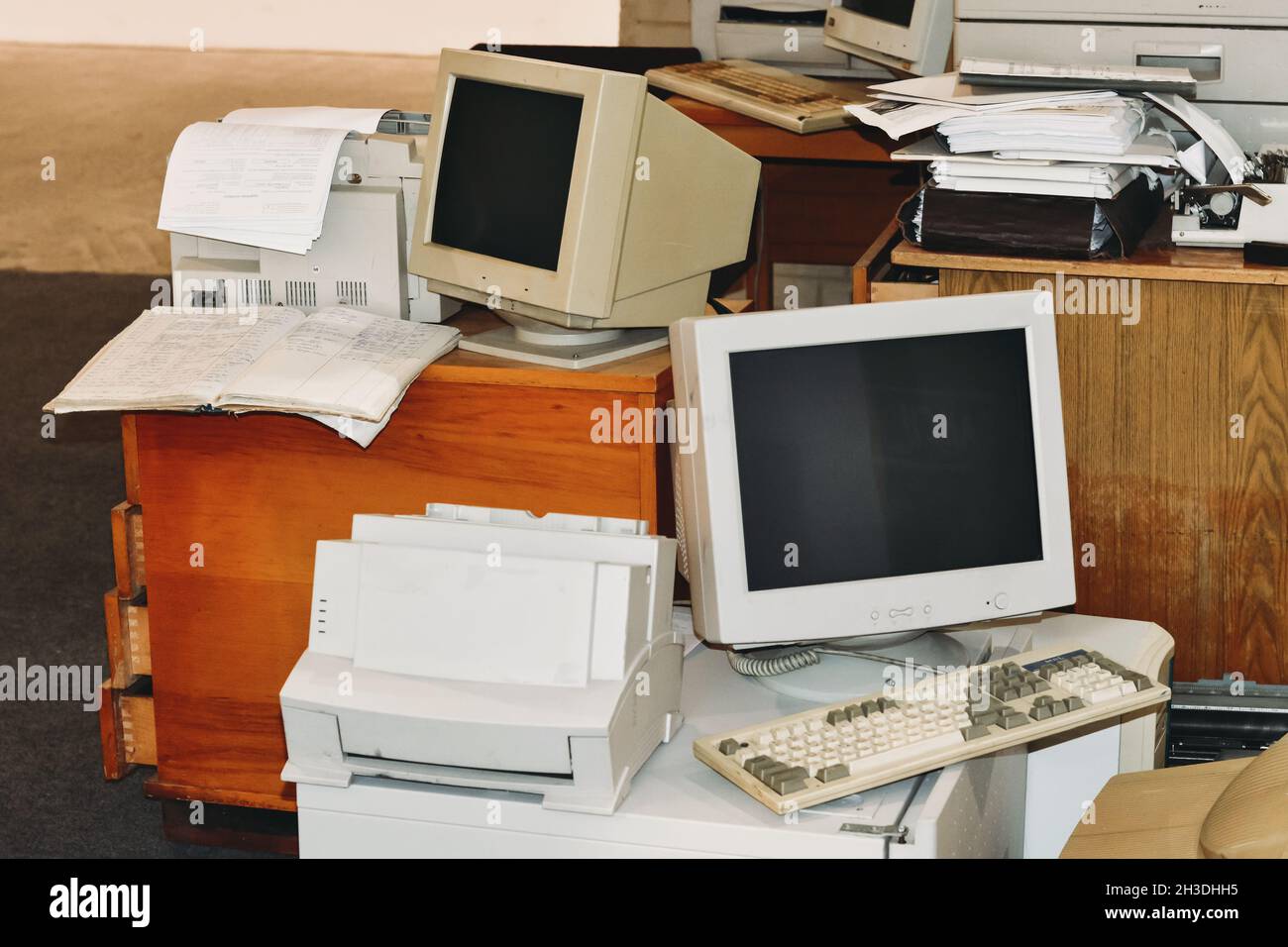 Ordenadores antiguos, impresoras, máquinas de escribir, teclados listos para la basura de la oficina. Dispositivo retro, pantallas y monitores en la mesa y el suelo Foto de stock