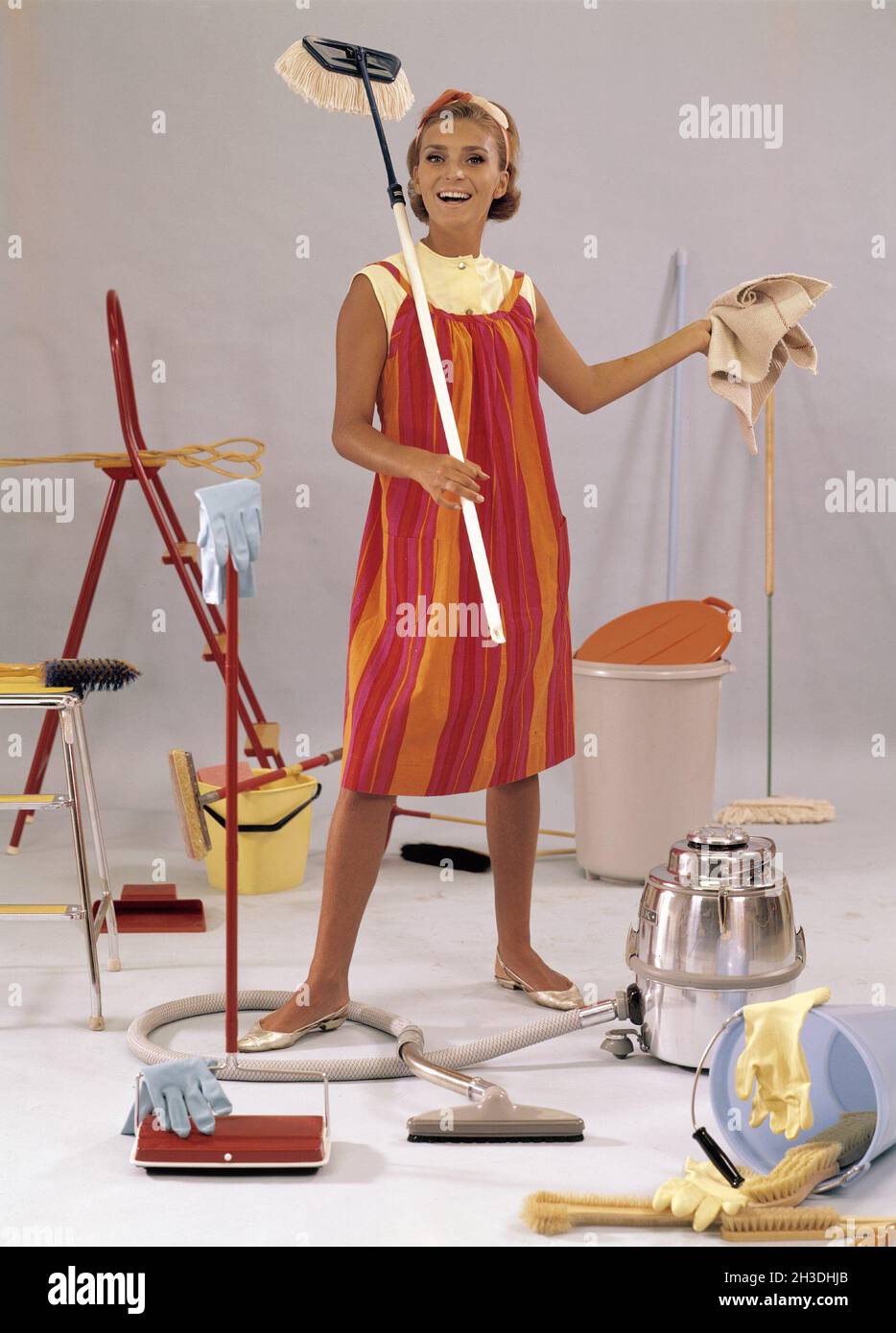 Día de limpieza en el 1960s. Una mujer joven se representa con mopas,  aspiradora, cubos, paños. Cosas y objetos típicamente usados en el 1960s al  limpiar la casa Fotografía de stock -