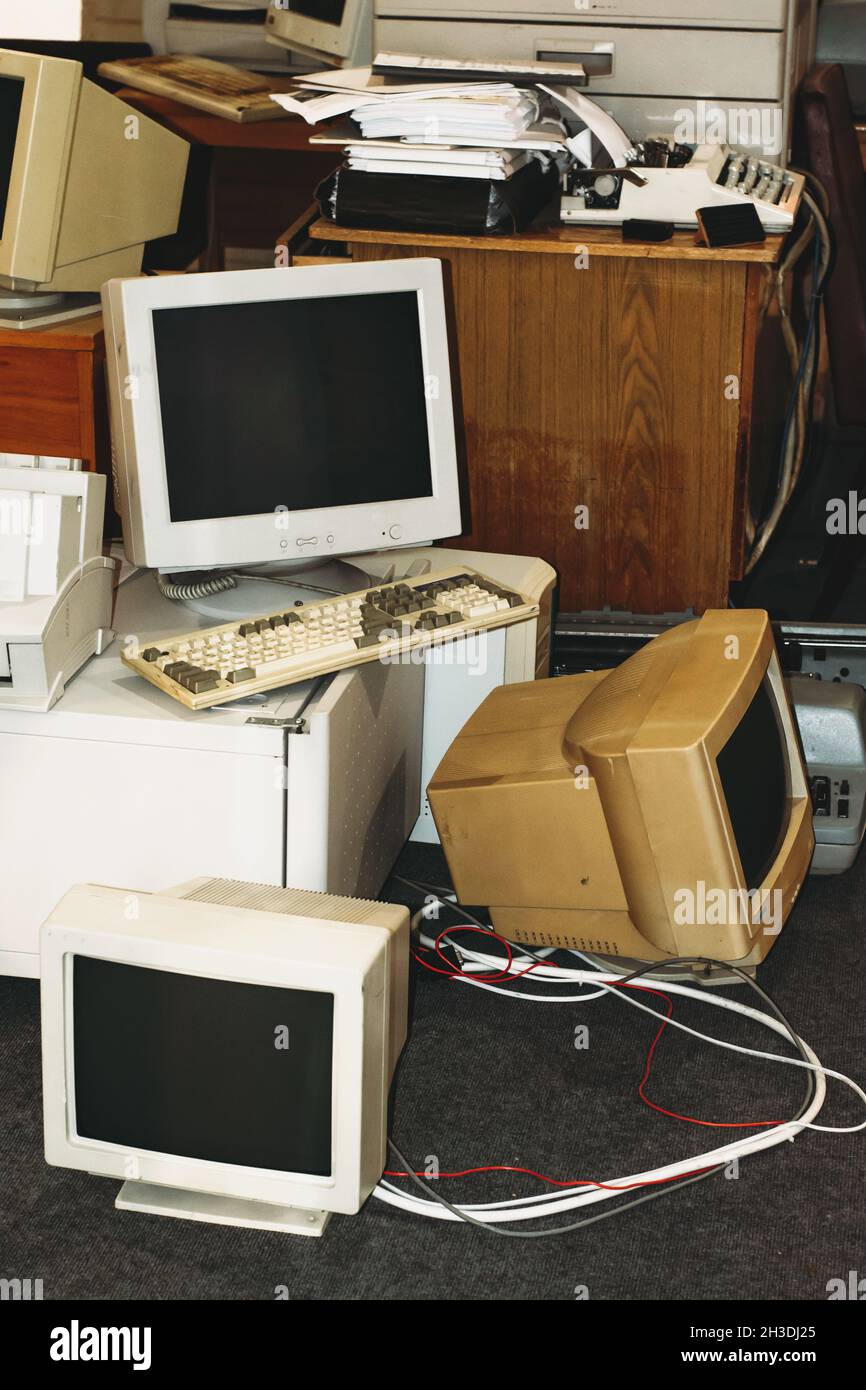 Ordenadores antiguos, impresoras, máquinas de escribir, teclados listos para la basura de la oficina. Dispositivo retro, pantallas y monitores en la mesa y el suelo Foto de stock