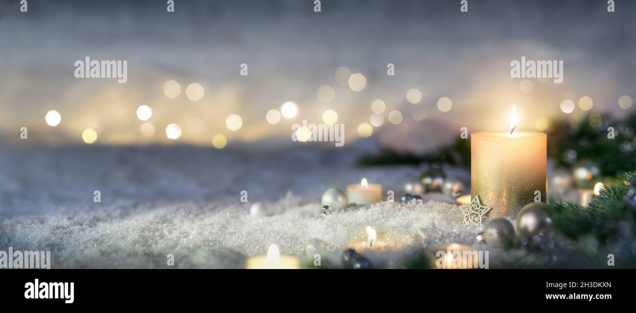 Decoración navideña con velas, luces, ramas de abeto y adornos en la nieve, formato panorámico Foto de stock