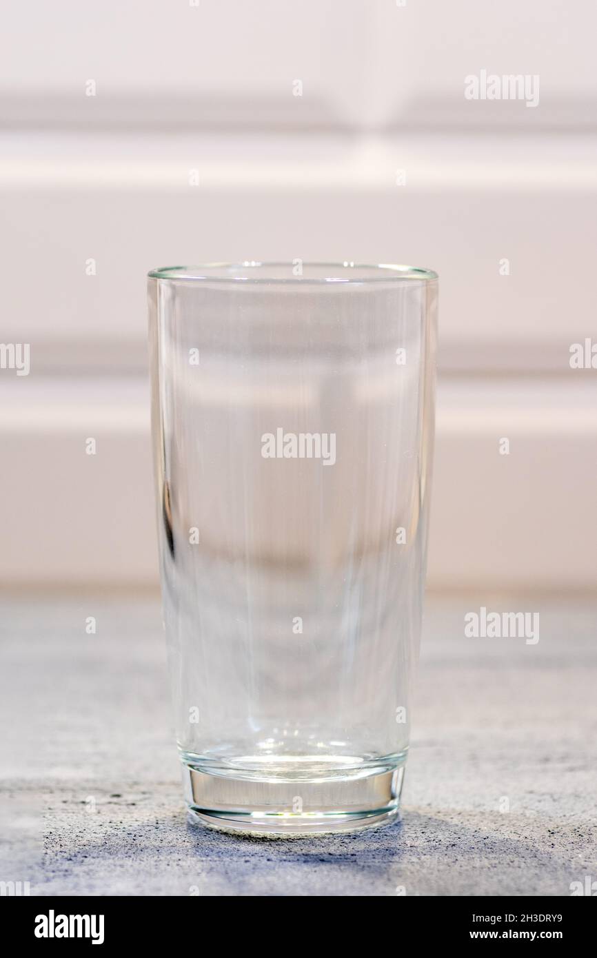 Gran vidrio transparente vacío sobre una mesa de madera azul en la cocina, primer plano. Un vaso de leche para el desayuno. El concepto de limpieza, washin Foto de stock