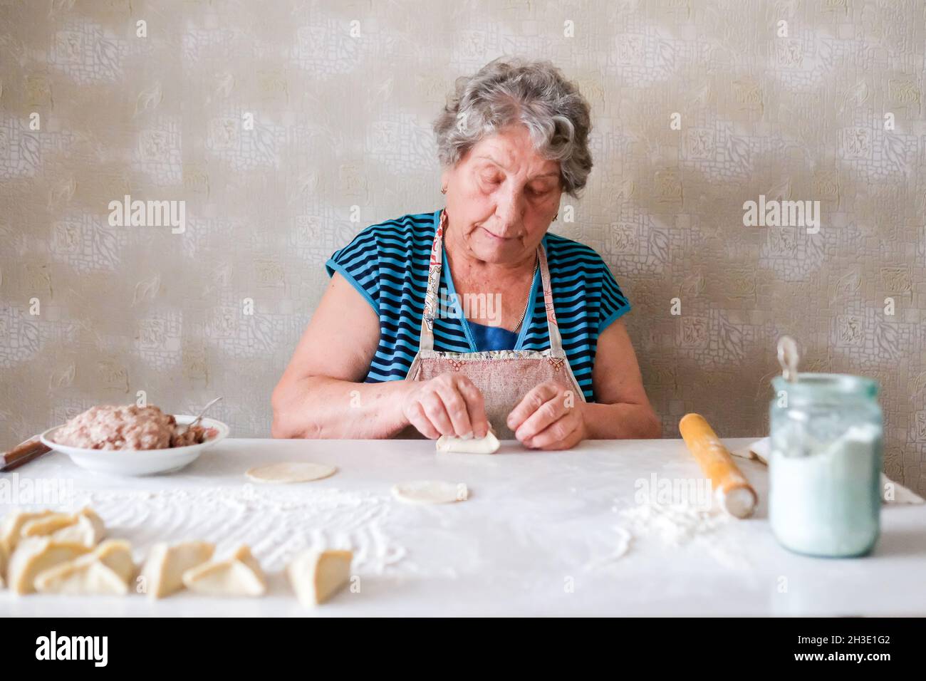 La abuela hace manti, esculpe un plato de masa Foto de stock