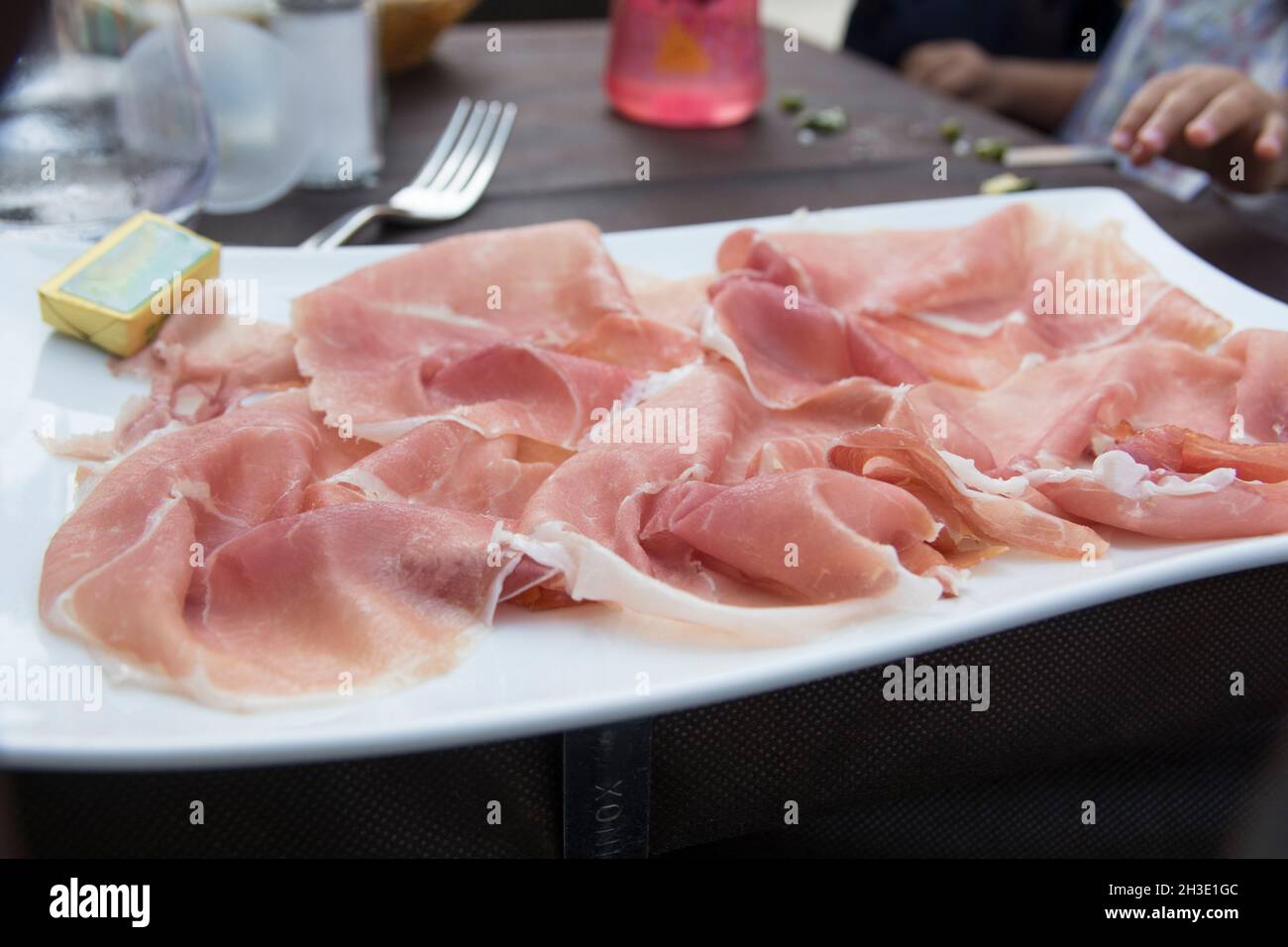 Prosciutto, un jamón italiano seco, cortado en rodajas finas y servido uncooked en un plato blanco Foto de stock