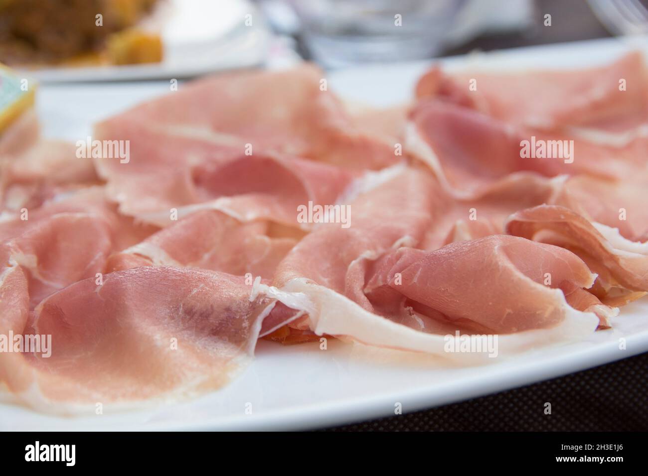 Prosciutto, un jamón italiano seco, cortado en rodajas finas y servido uncooked en un plato blanco Foto de stock