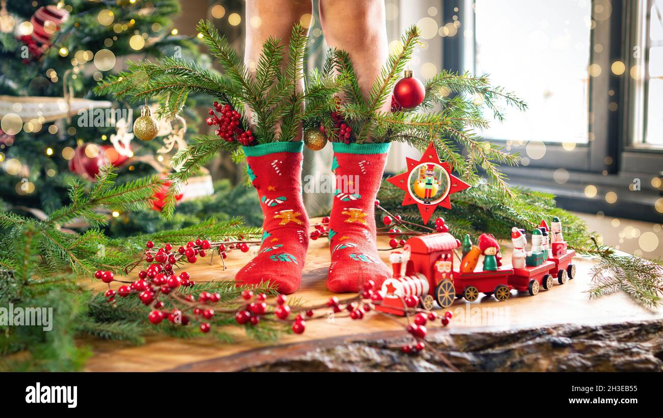 Pies de niño en calcetines decorados con ramas de árbol de Navidad,  juguetes, pelotas. Una foto navideña con un ambiente cálido y un ambiente  festivo para un saludo Fotografía de stock -