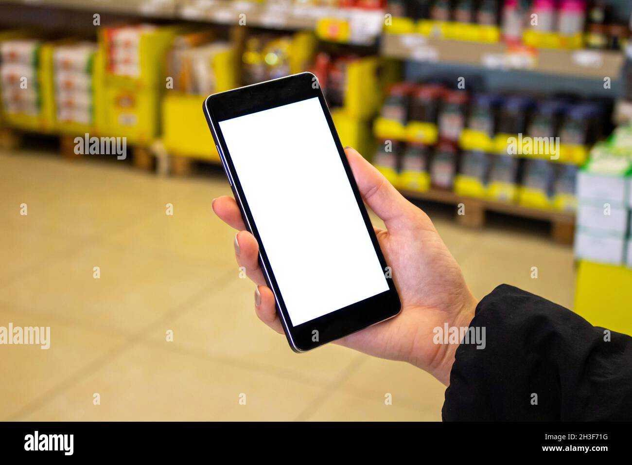 Mujer usando el teléfono móvil, burla imagen de la mano femenina sosteniendo el teléfono móvil con pantalla blanca en el supermercado. Foto de stock