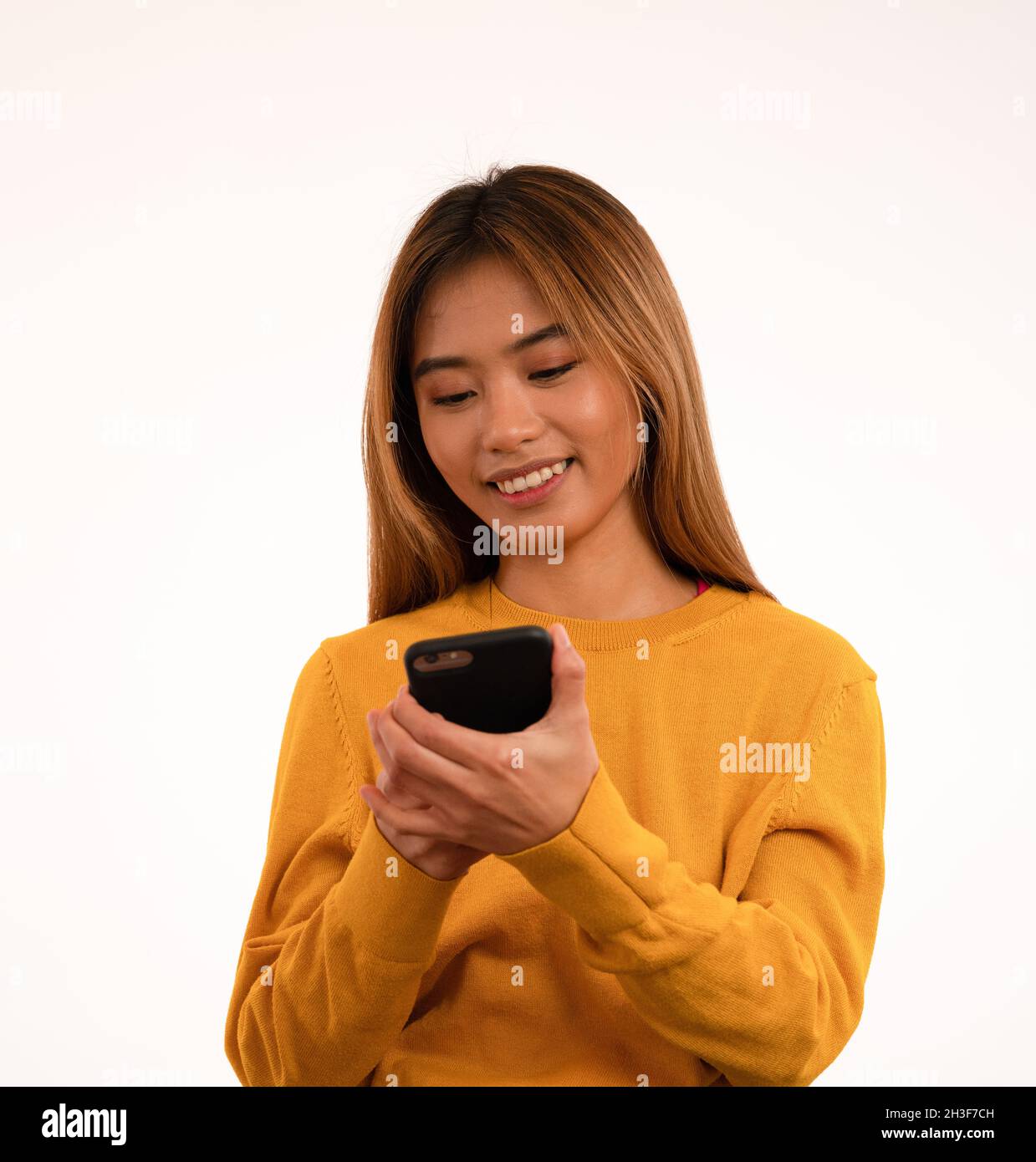 Joven atractiva chica asiática sonriendo mientras se utiliza el smartphone en el estudio Foto de stock