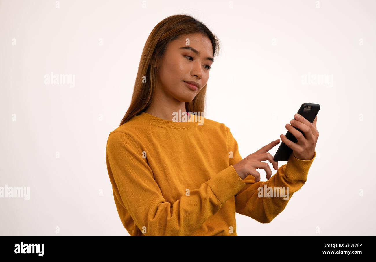 Joven atractiva chica asiática sonriendo mientras se utiliza el smartphone en el estudio Foto de stock