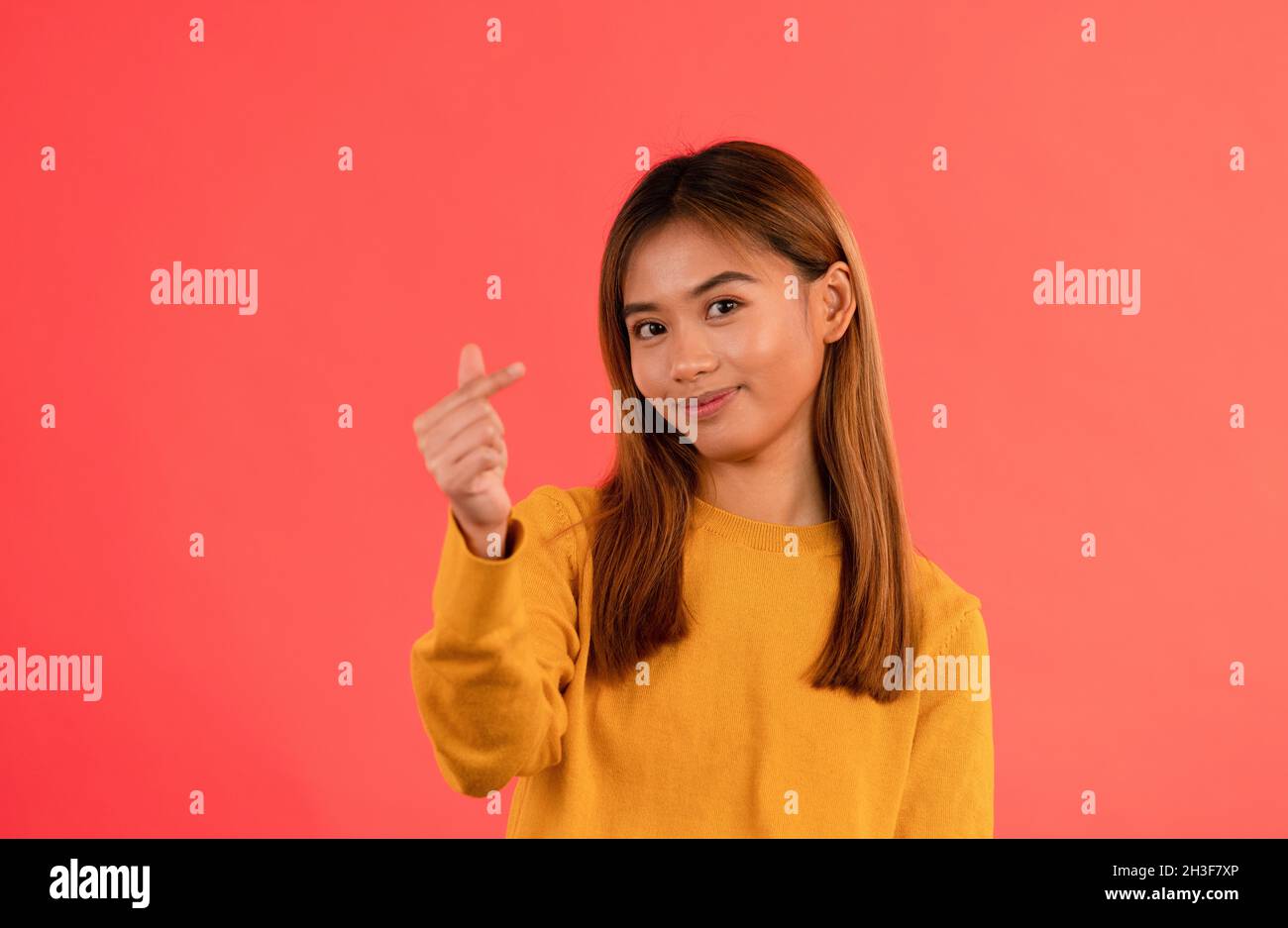 Joven atractiva chica asiática sonriendo con el dedo del corazón en el estudio Foto de stock