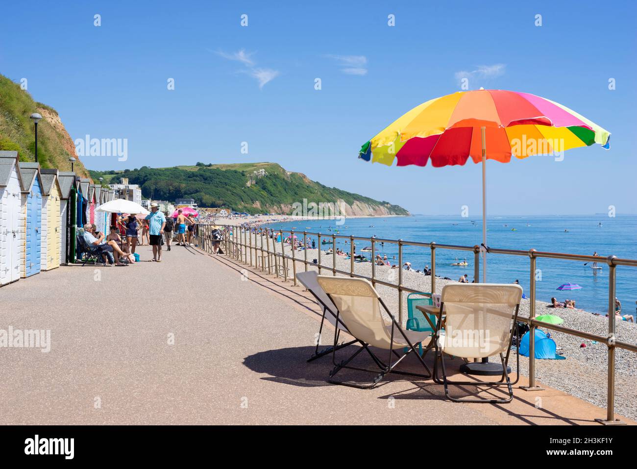 Seaton Devon Gente tomando el sol y usando sombrillas de playa en las cabañas de playa a lo largo del paseo marítimo en Seaton Devon Inglaterra Reino Unido GB Europa Foto de stock