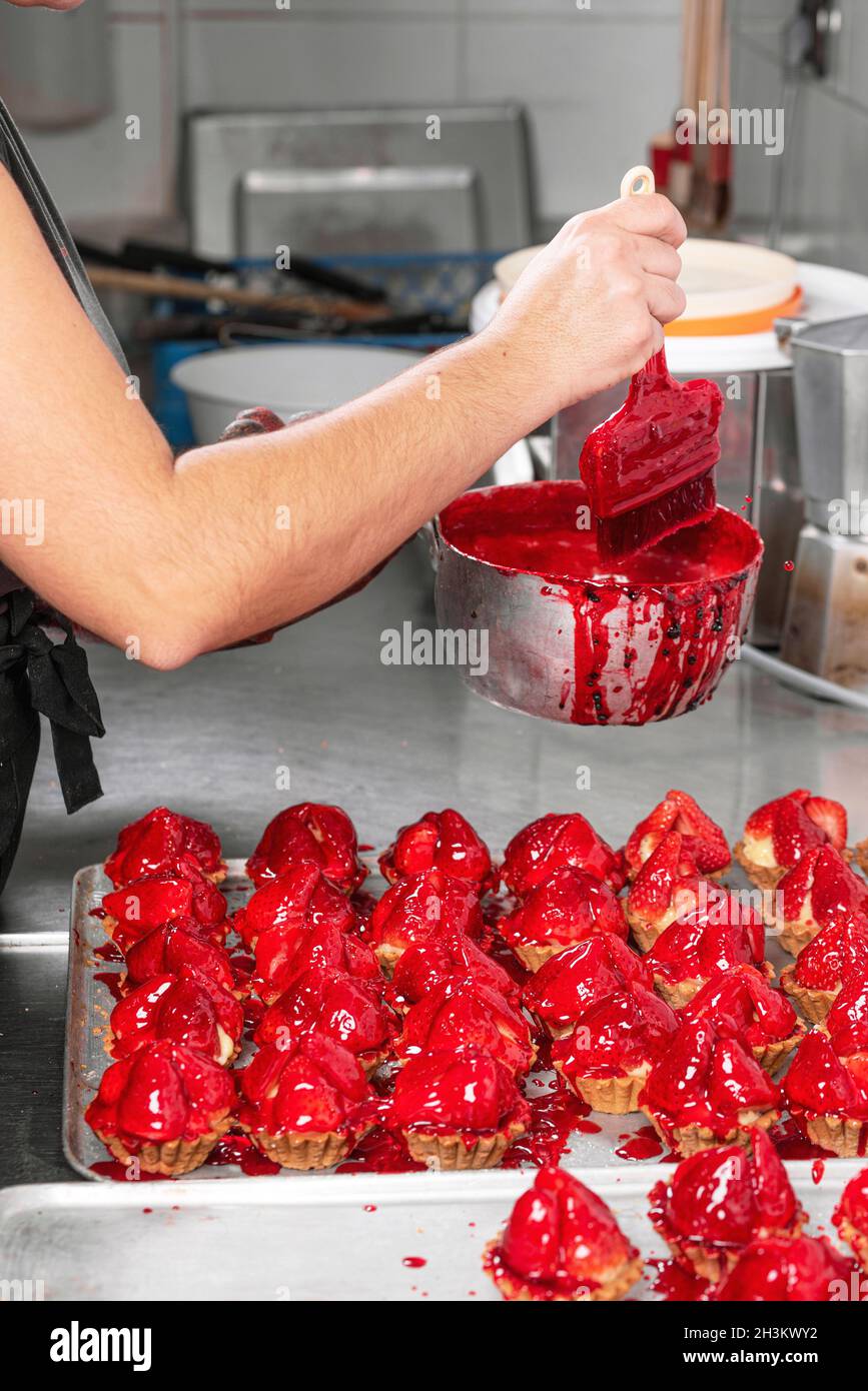 El confitero hace pasteles con fresas frescas en un tartlet. Foto de stock