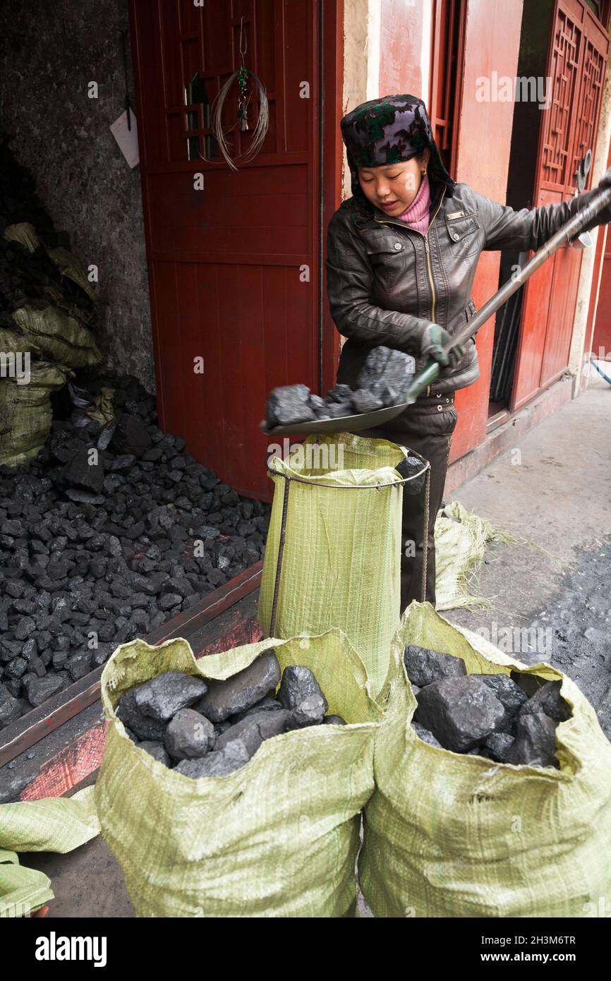 Mujer musulmana con pala embolsando carbón en sacos para la venta o el uso,  dentro de la antigua ciudad amurallada china (antigua ciudad amurallada) de  Songpan en ninguna provincia del norte de