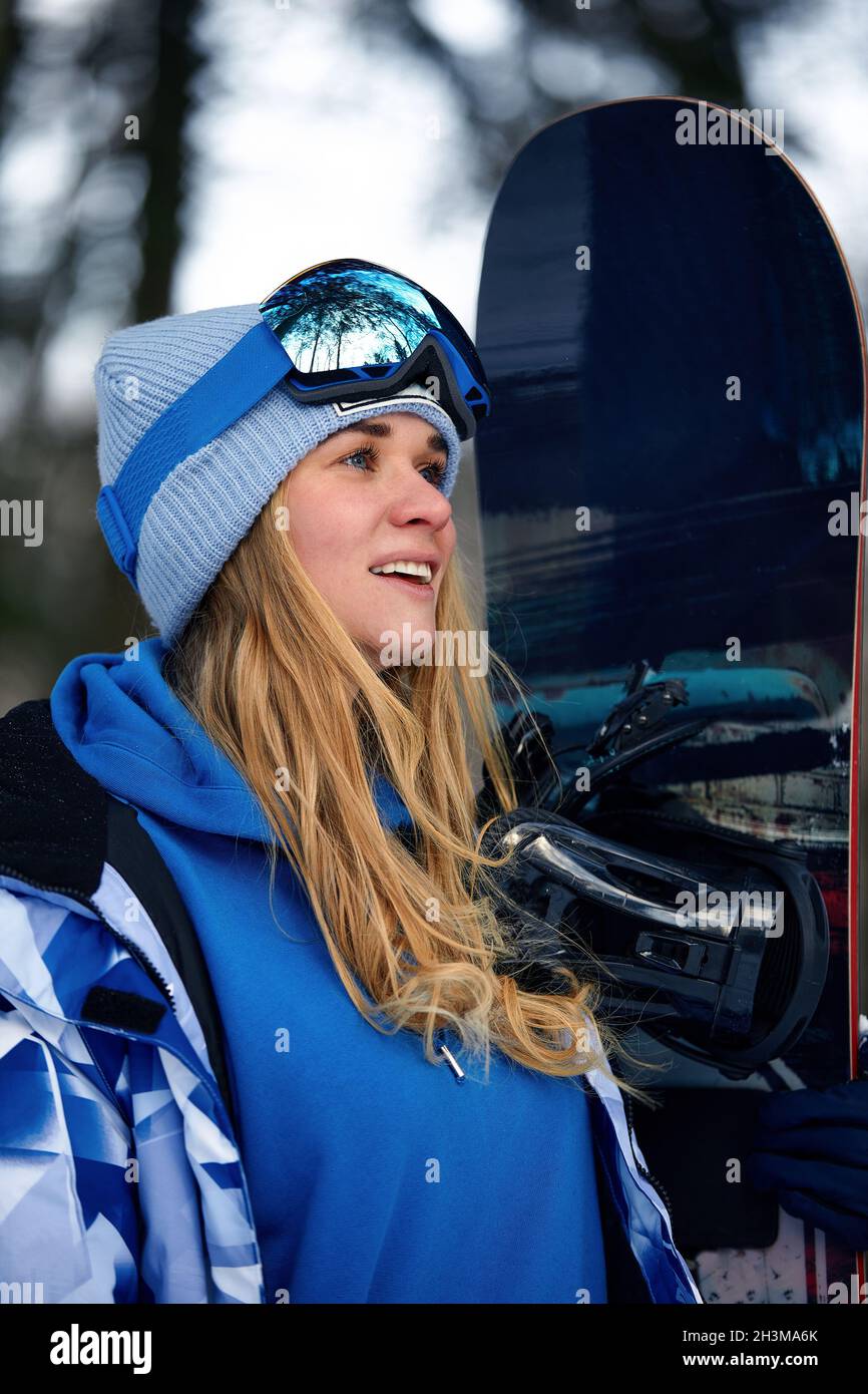 imagen con un retrato de una snowboarder mujer con casco con un reflejo brillante en las gafas sobre el fondo de la montaña de nieve alta. Foto de stock