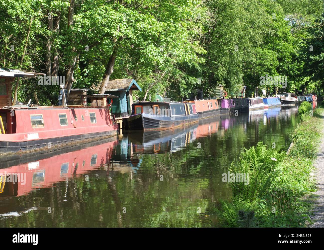 Barcos antiguos del canal amarrados en el canal rochdale cerca del puente hebden rodeado de árboles bajo la luz del sol en verano Foto de stock