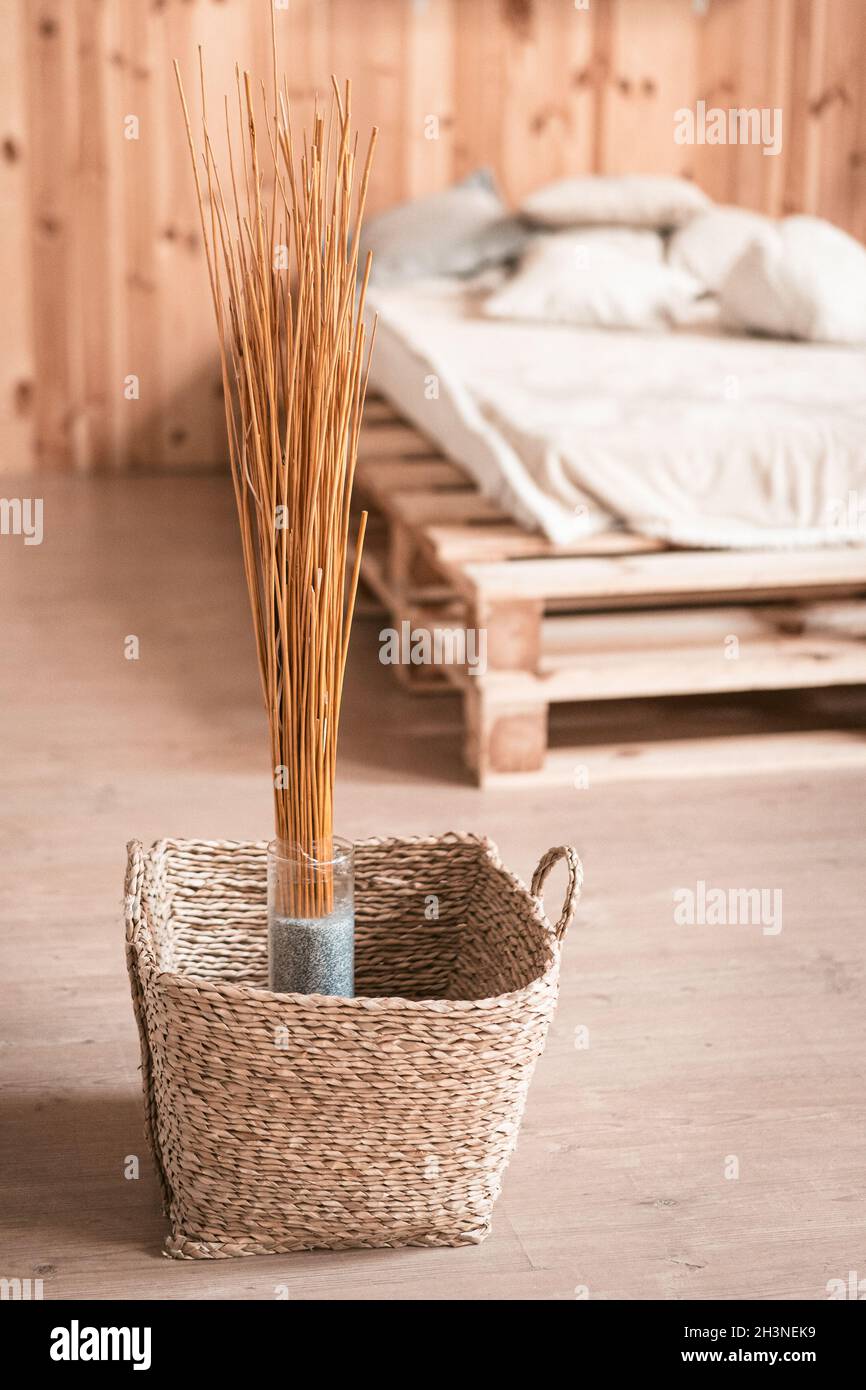 Decoración natural en el interior de madera del dormitorio. Ramo de palos secos en jarrón y cesta de mimbre en el suelo Foto de stock