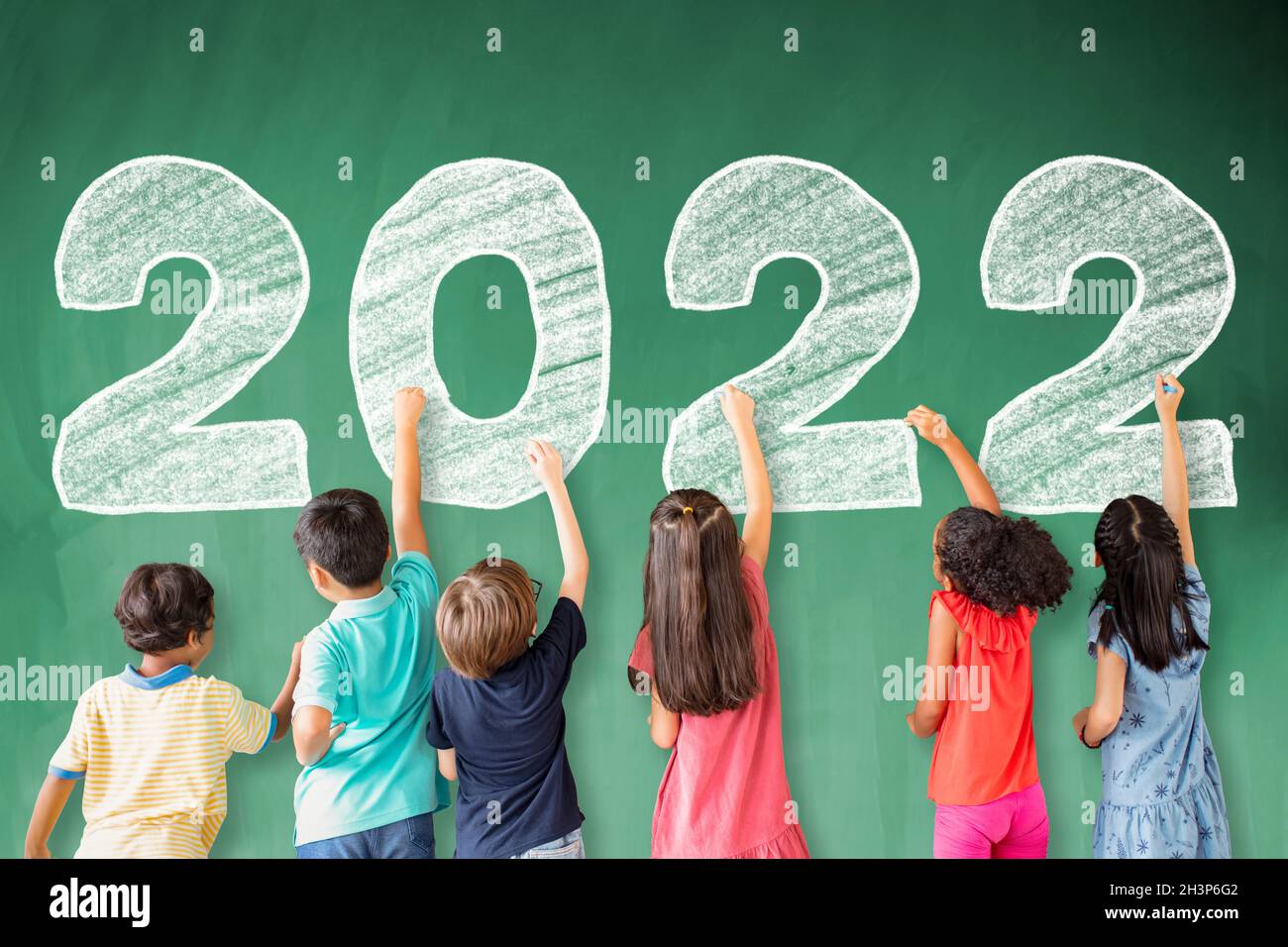 Los niños escolares sacan el año nuevo 2022 en la pizarra. Foto de stock