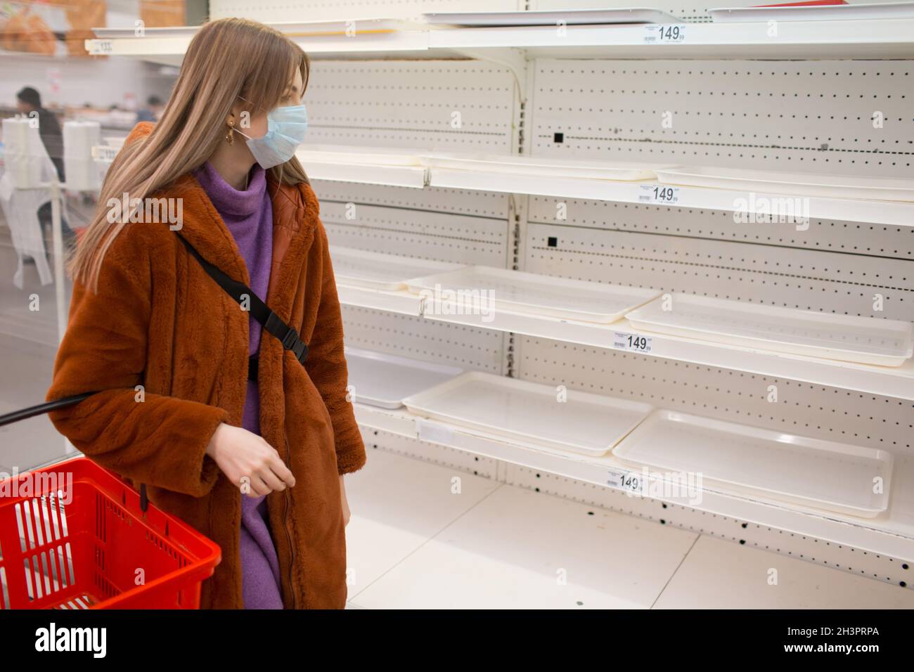 Mujer joven en mascarilla médica y estanterías vacías en el supermercado. Foto de stock