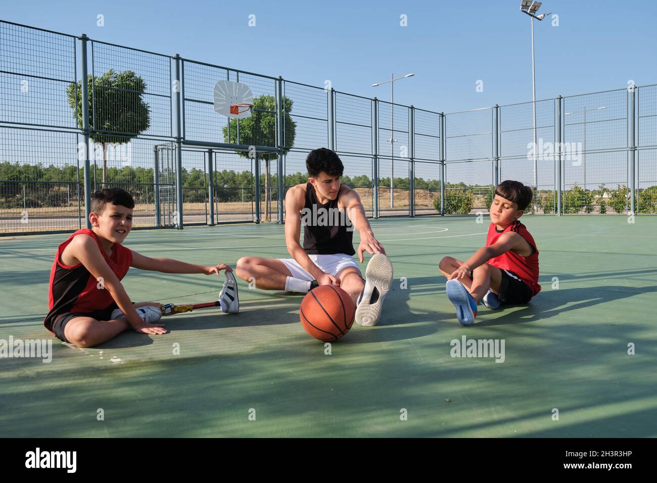 Entrenador de baloncesto haciendo ejercicios de estiramiento de piernas con dos niños. Foto de stock
